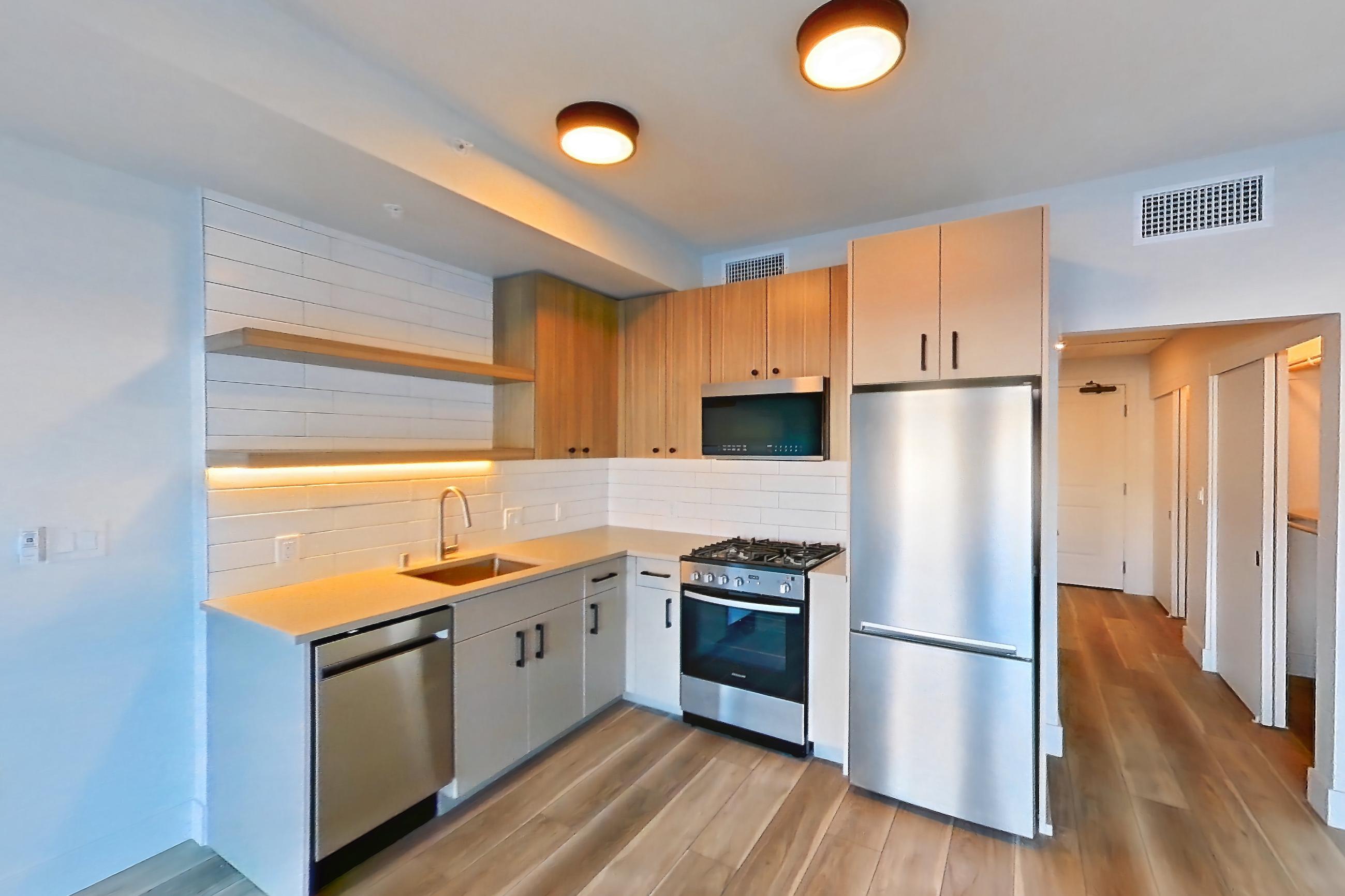 Living space with dishwasher, gas range, light countertops, light wood-finish flooring, oven/range, refrigerator, and stainless steel appliances, Apartment 253 at The Myles