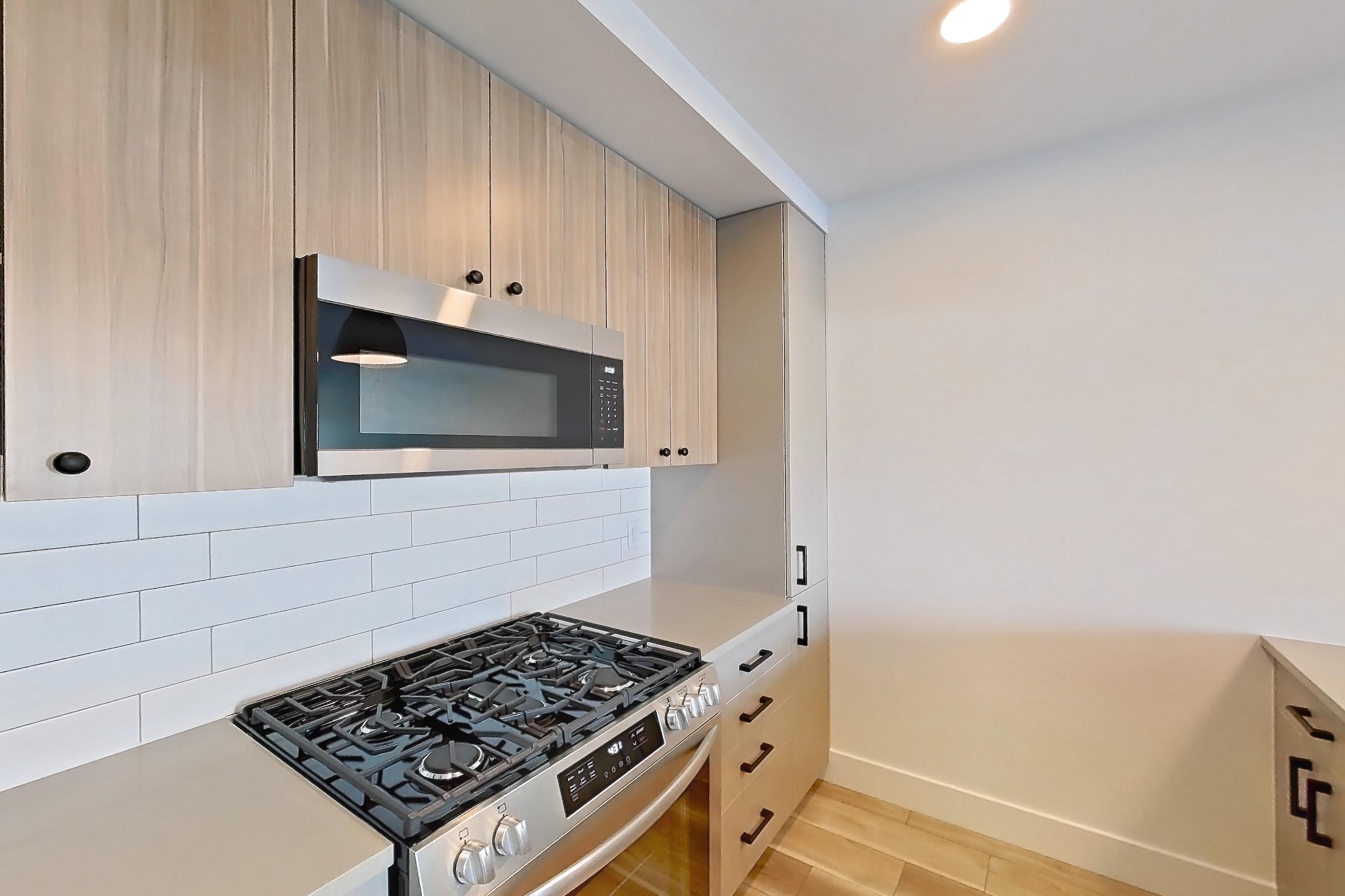 Kitchen with dishwasher, gas range, light countertops, light wood-finish flooring, oven/range, refrigerator, and stainless steel appliances, Apartment 255 at The Myles