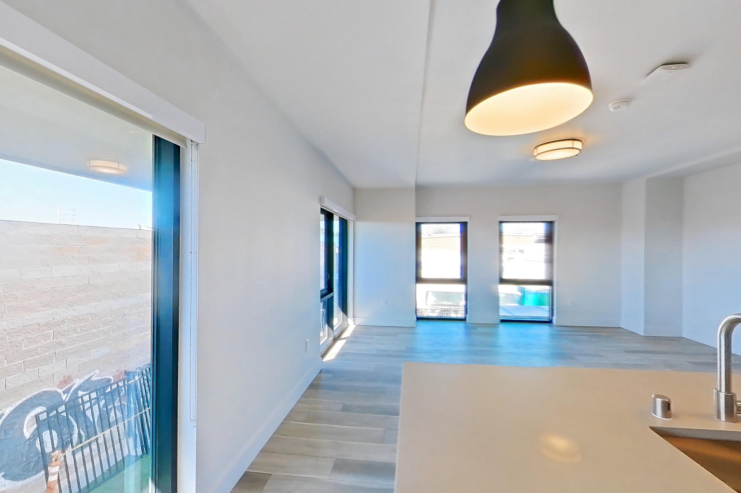 Kitchen with dishwasher, gas range, kitchen island, light countertops, light stone countertops, light wood-finish flooring, microwave, oven/range, refrigerator, and stainless steel appliances, Apartment 258 at The Myles