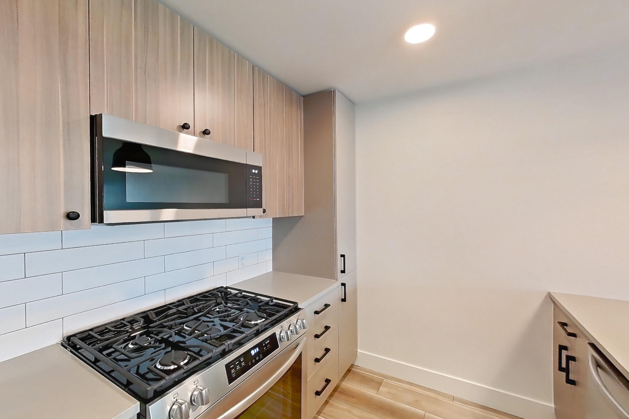 Kitchen with dishwasher, gas range, light countertops, light wood-finish flooring, microwave, oven/range, refrigerator, and stainless steel appliances, Apartment 311 at The Myles