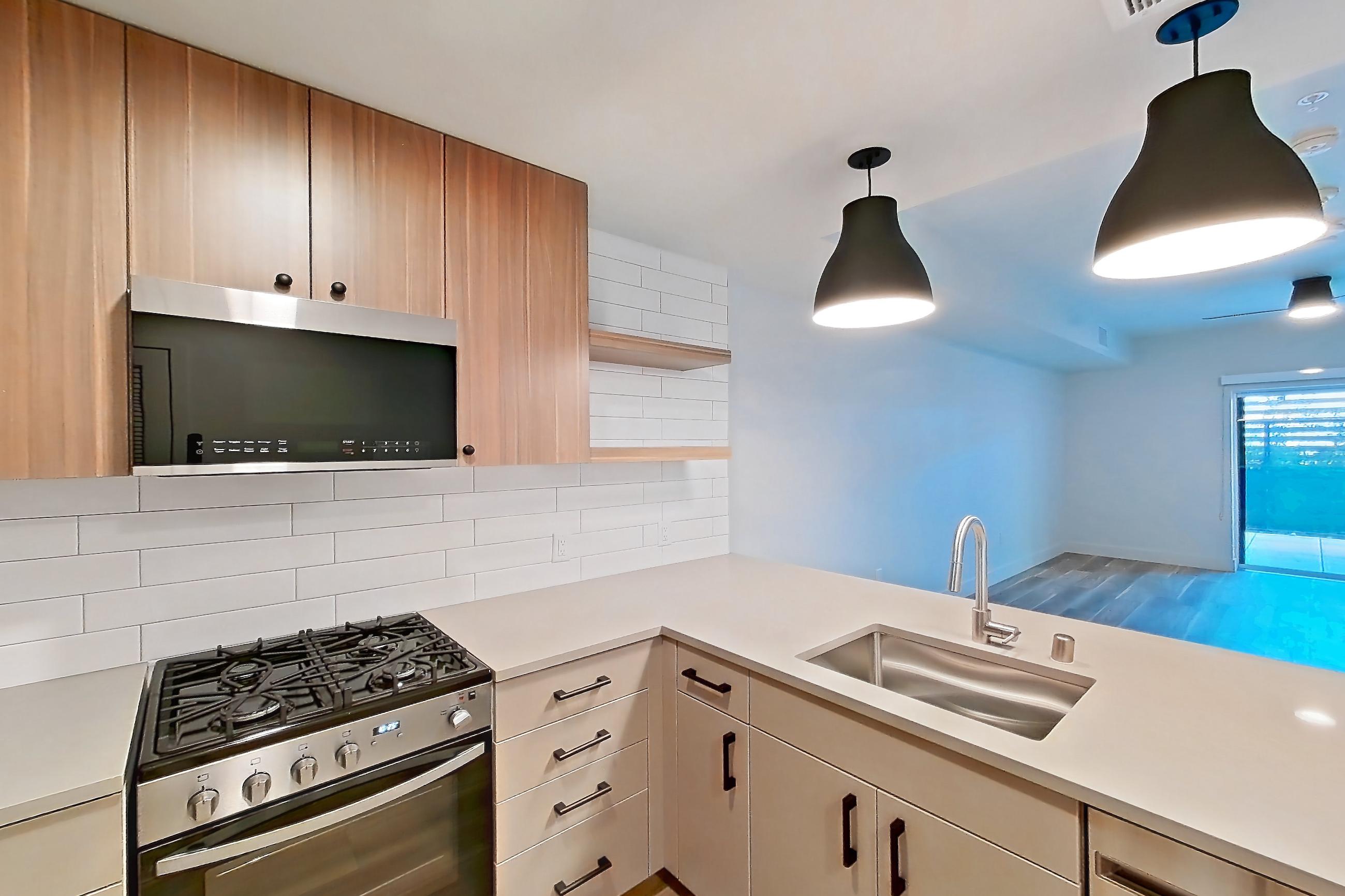 Kitchen with gas range, light countertops, light wood-finish flooring, oven/range, refrigerator, and stainless steel appliances, Apartment 319 at The Myles