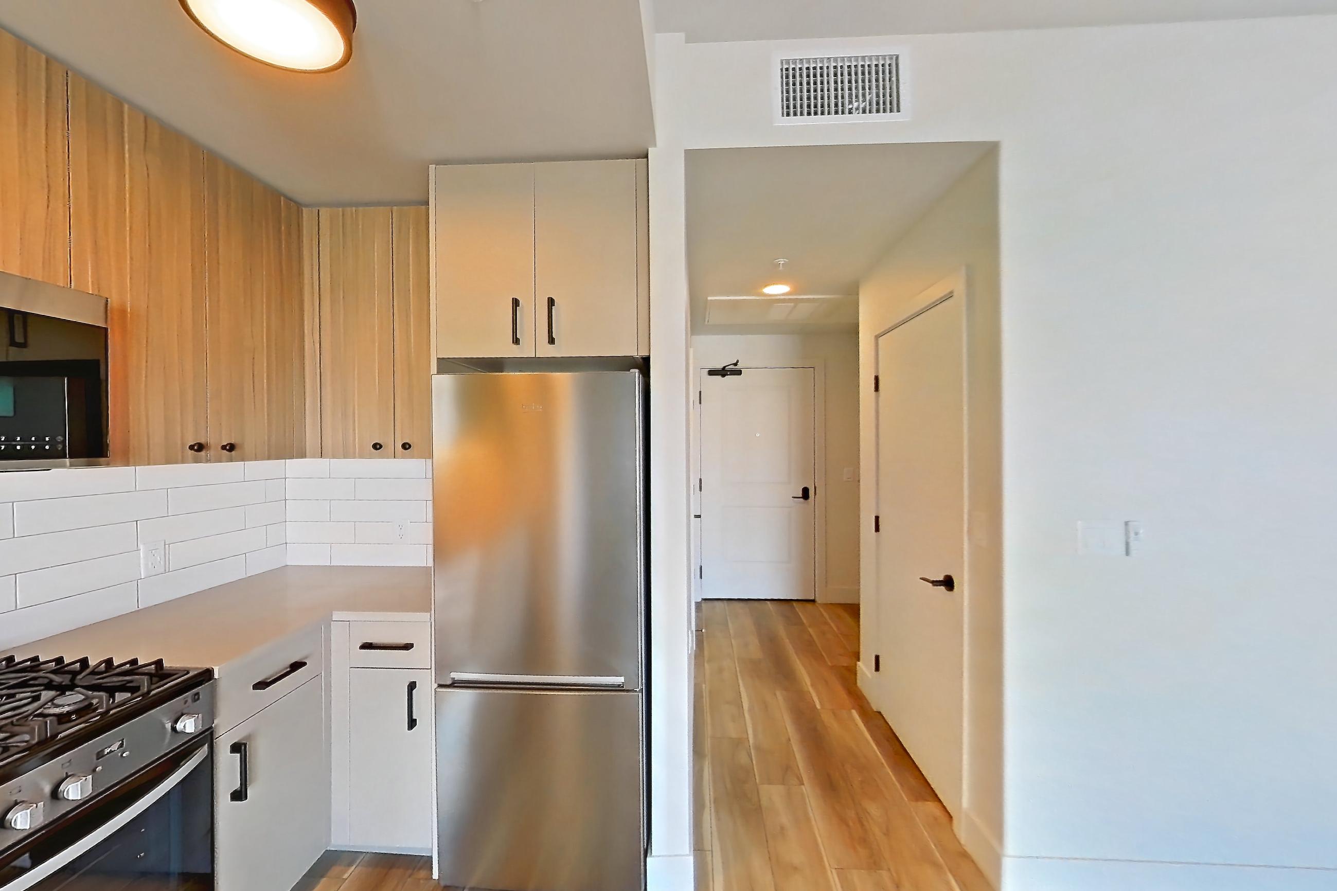 Kitchen with gas range, light countertops, light wood-finish flooring, oven/range, refrigerator, and stainless steel appliances, Apartment 320 at The Myles