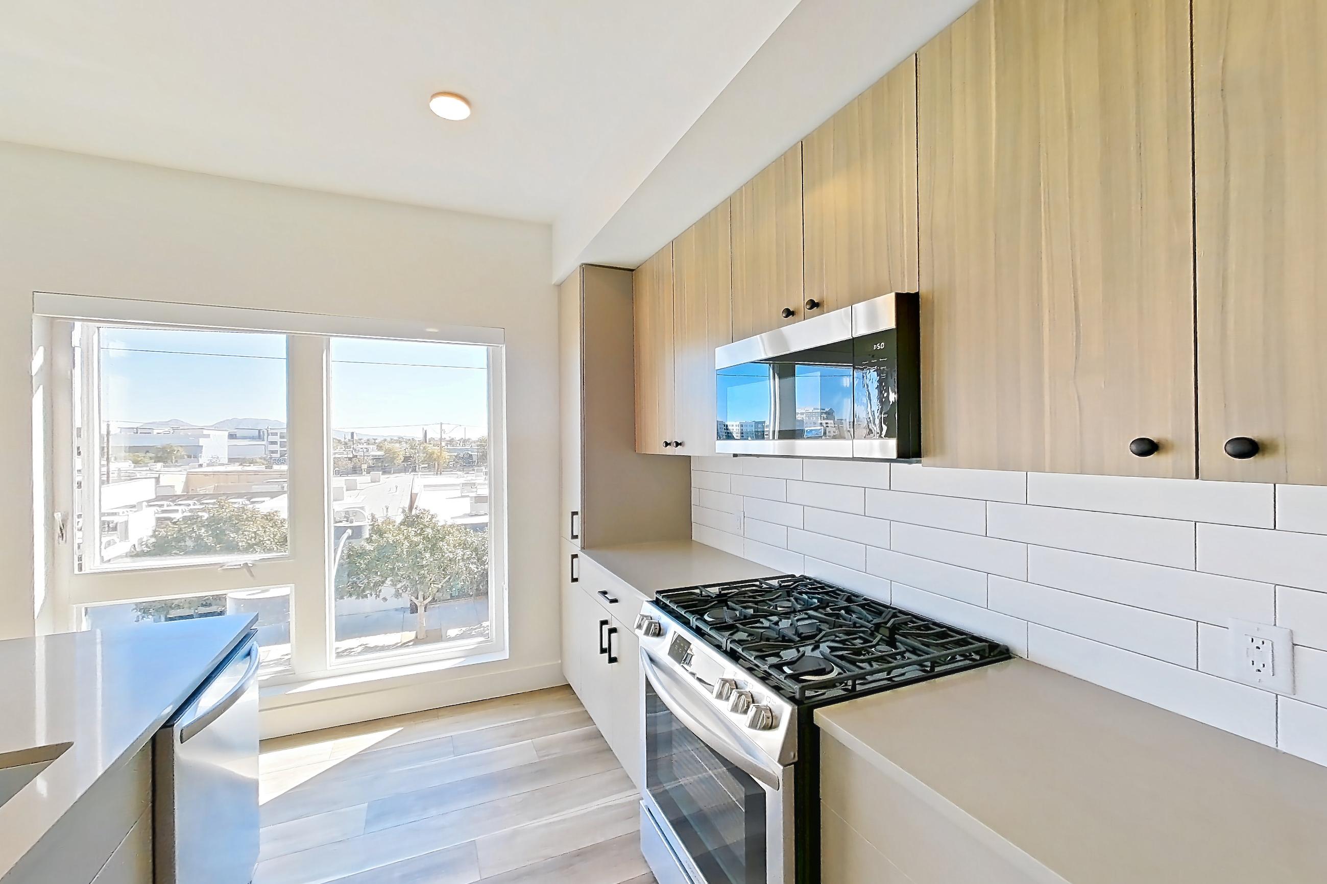 Kitchen with gas range, kitchen island, light countertops, light wood-finish flooring, oven/range, and stainless steel appliances, Apartment 324 at The Myles