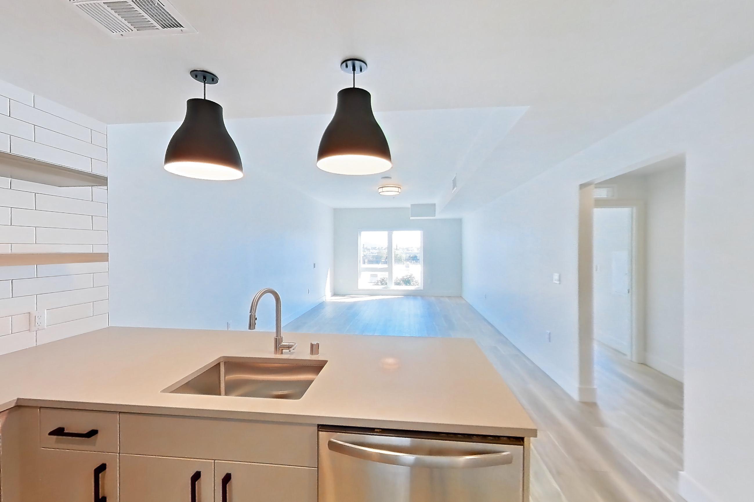 Kitchen with dishwasher, gas range, light countertops, light stone countertops, light wood-finish flooring, microwave, oven/range, refrigerator, and stainless steel appliances, Apartment 325 at The Myles