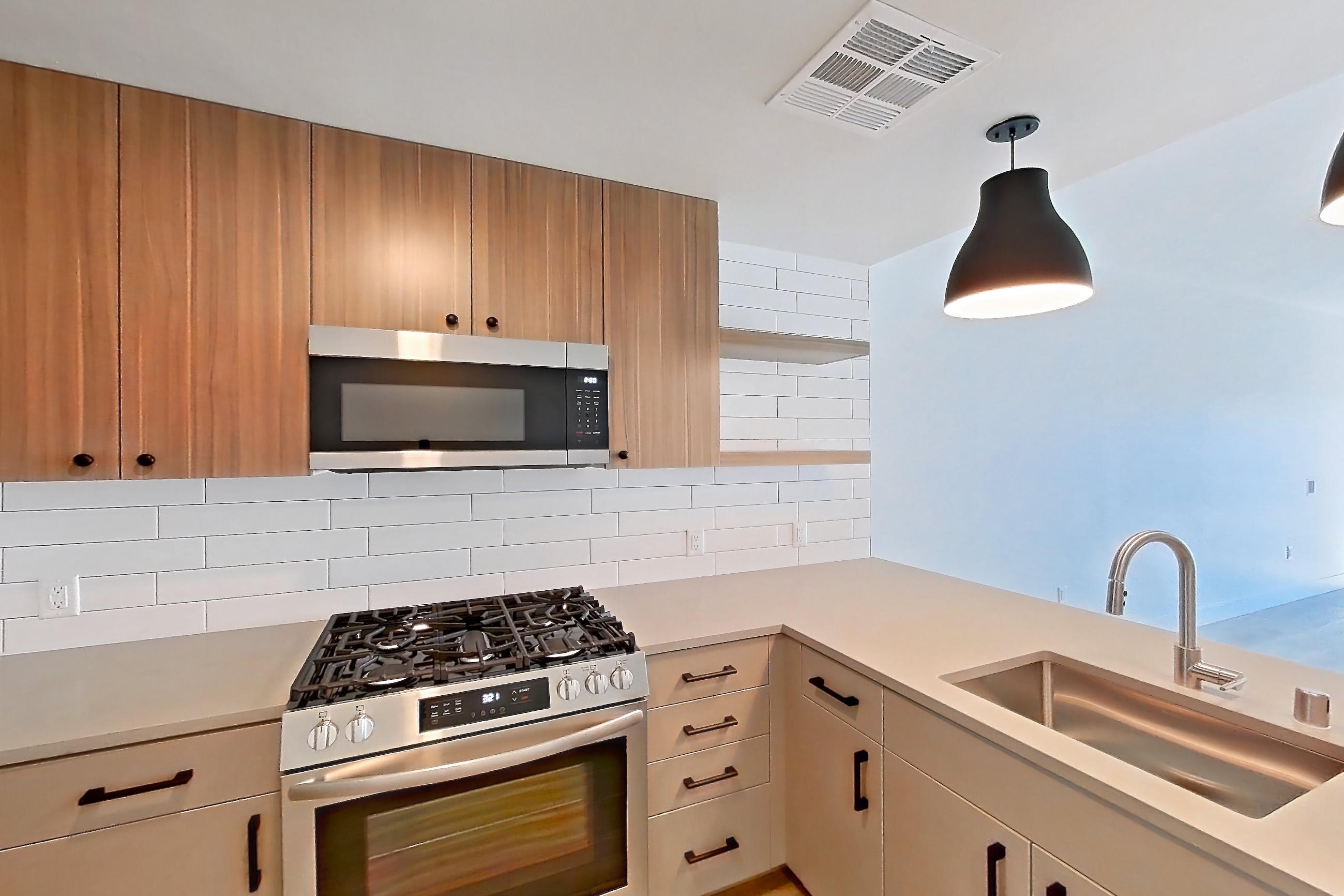 Kitchen with dishwasher, gas range, light countertops, light stone countertops, light wood-finish flooring, microwave, oven/range, refrigerator, and stainless steel appliances, Apartment 325 at The Myles