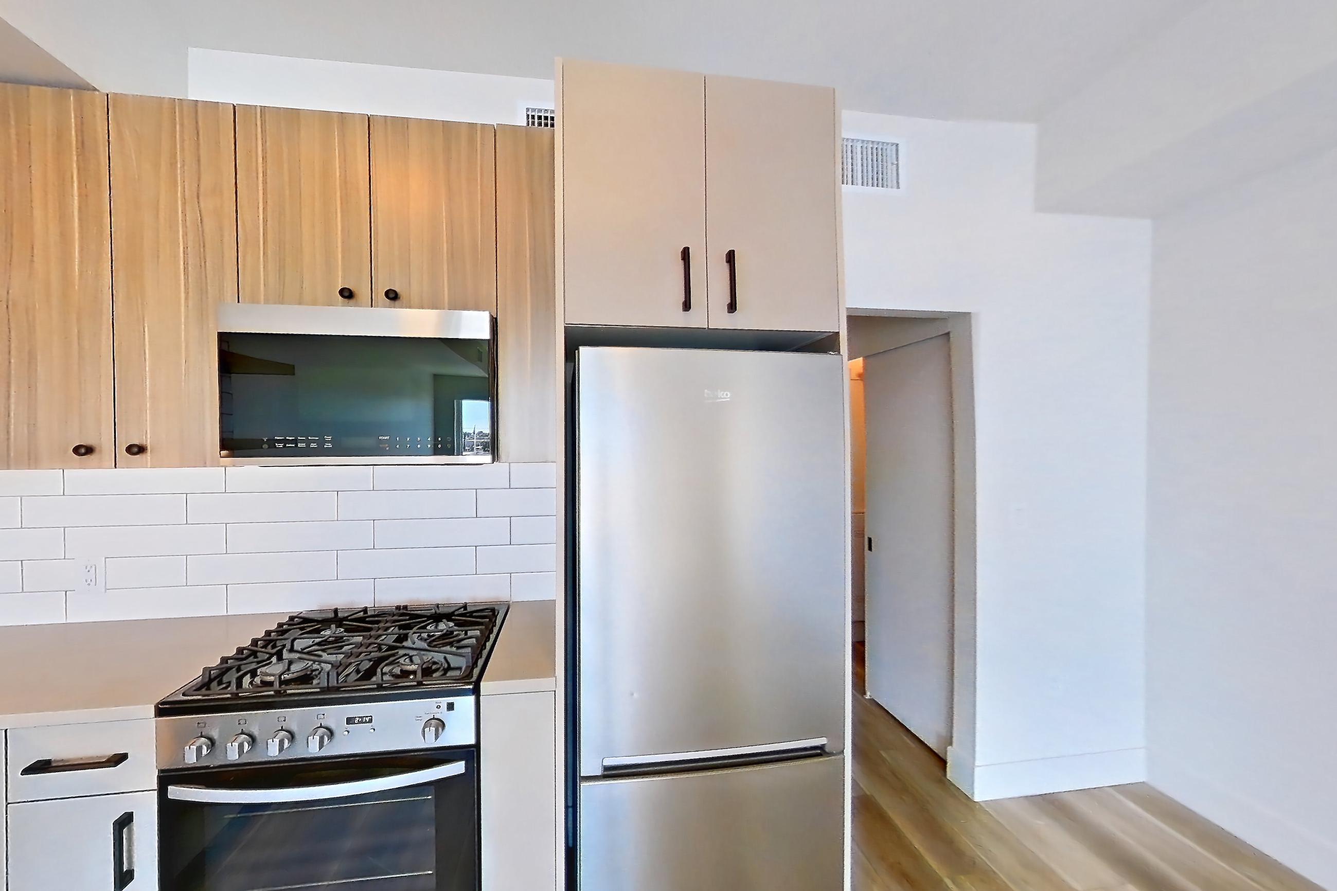 Kitchen with dishwasher, gas range, light countertops, light wood-finish flooring, oven/range, refrigerator, and stainless steel appliances, Apartment 326 at The Myles