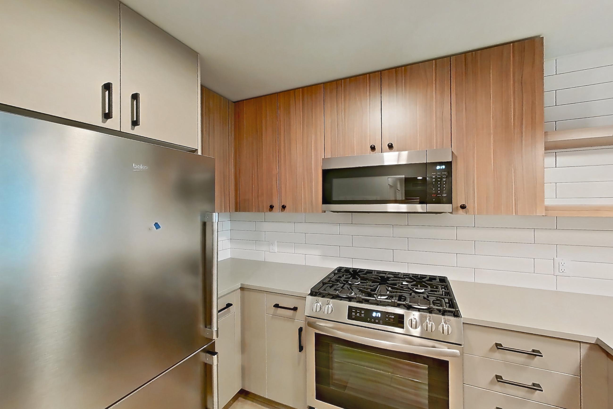 Kitchen with dishwasher, gas range, light countertops, light wood-finish flooring, microwave, oven/range, refrigerator, and stainless steel appliances, Apartment 327 at The Myles