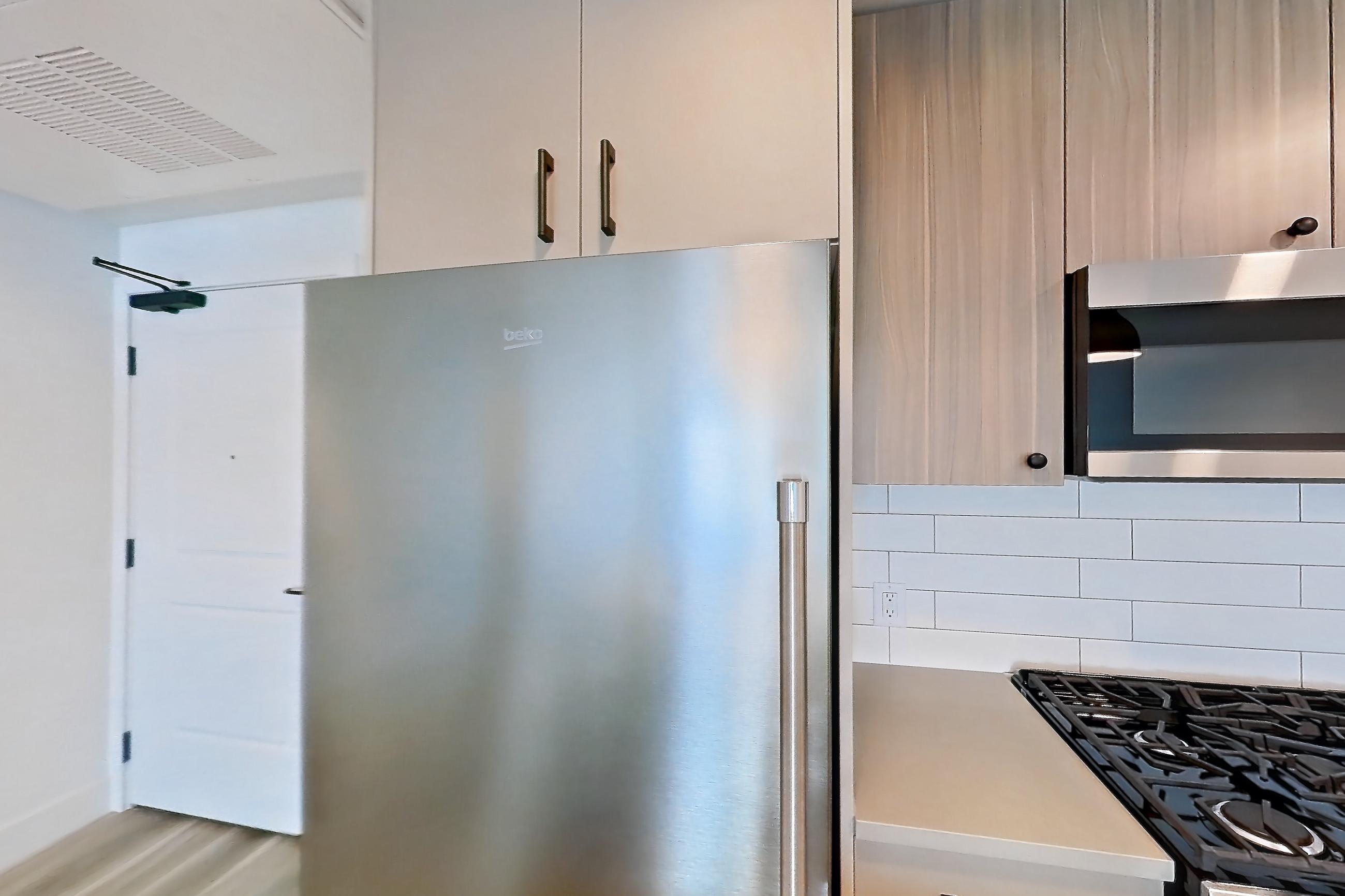 Kitchen with dishwasher, gas range, light countertops, light wood-finish flooring, microwave, oven/range, refrigerator, and stainless steel appliances, Apartment 330 at The Myles