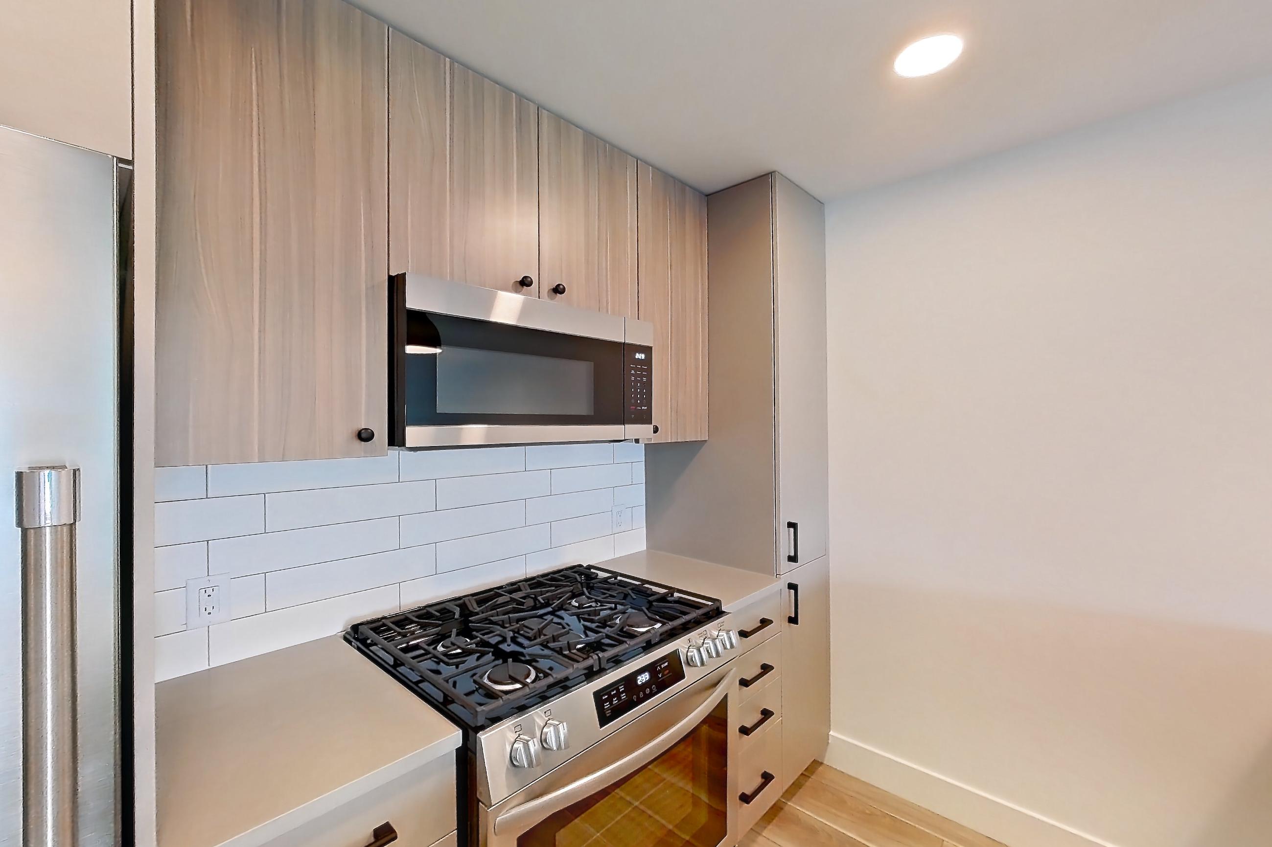 Kitchen with dishwasher, gas range, light countertops, light wood-finish flooring, microwave, oven/range, refrigerator, and stainless steel appliances, Apartment 330 at The Myles