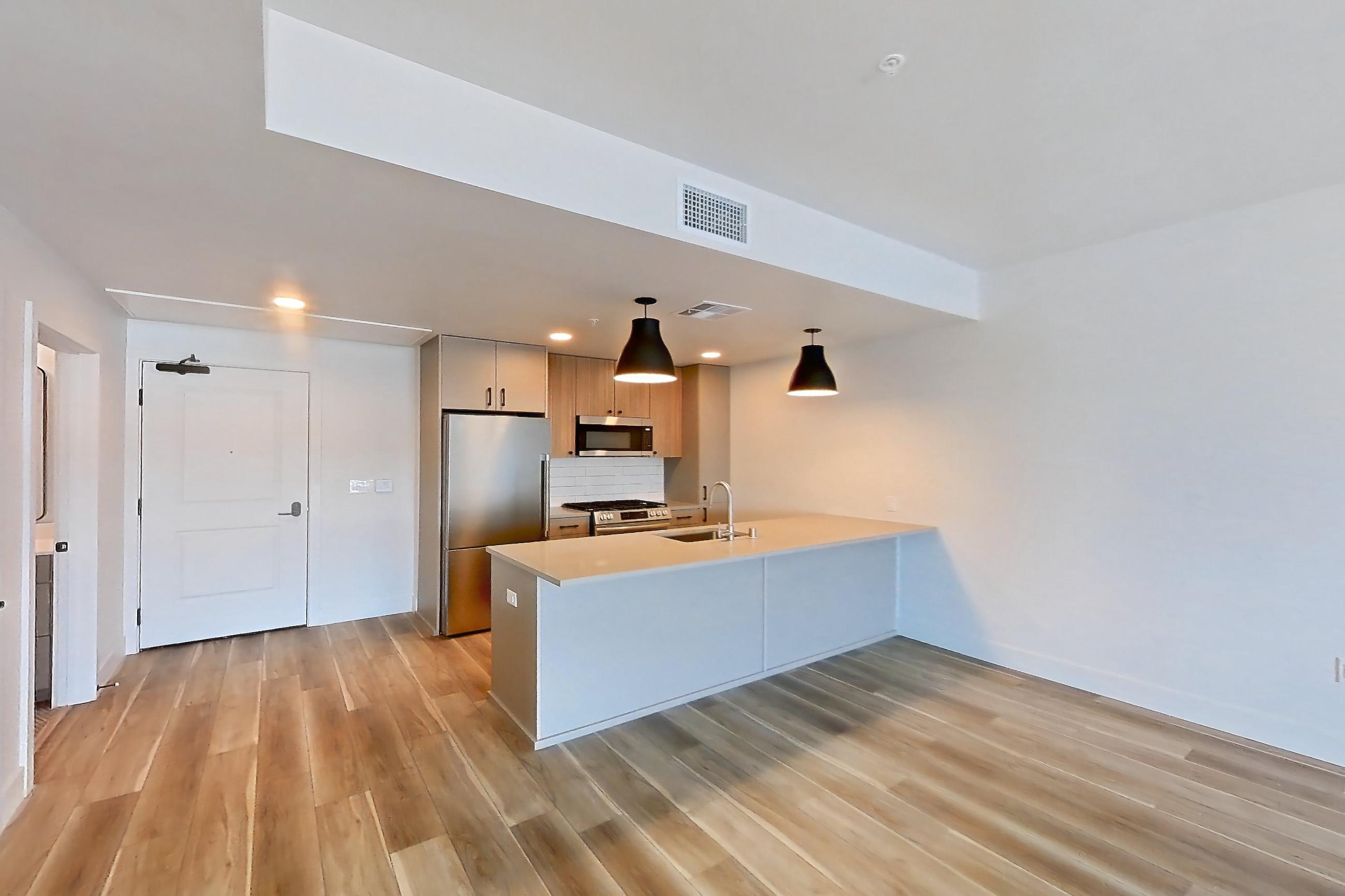 Living room with gas range, light countertops, light wood-finish flooring, oven/range, refrigerator, and stainless steel appliances, Apartment 330 at The Myles