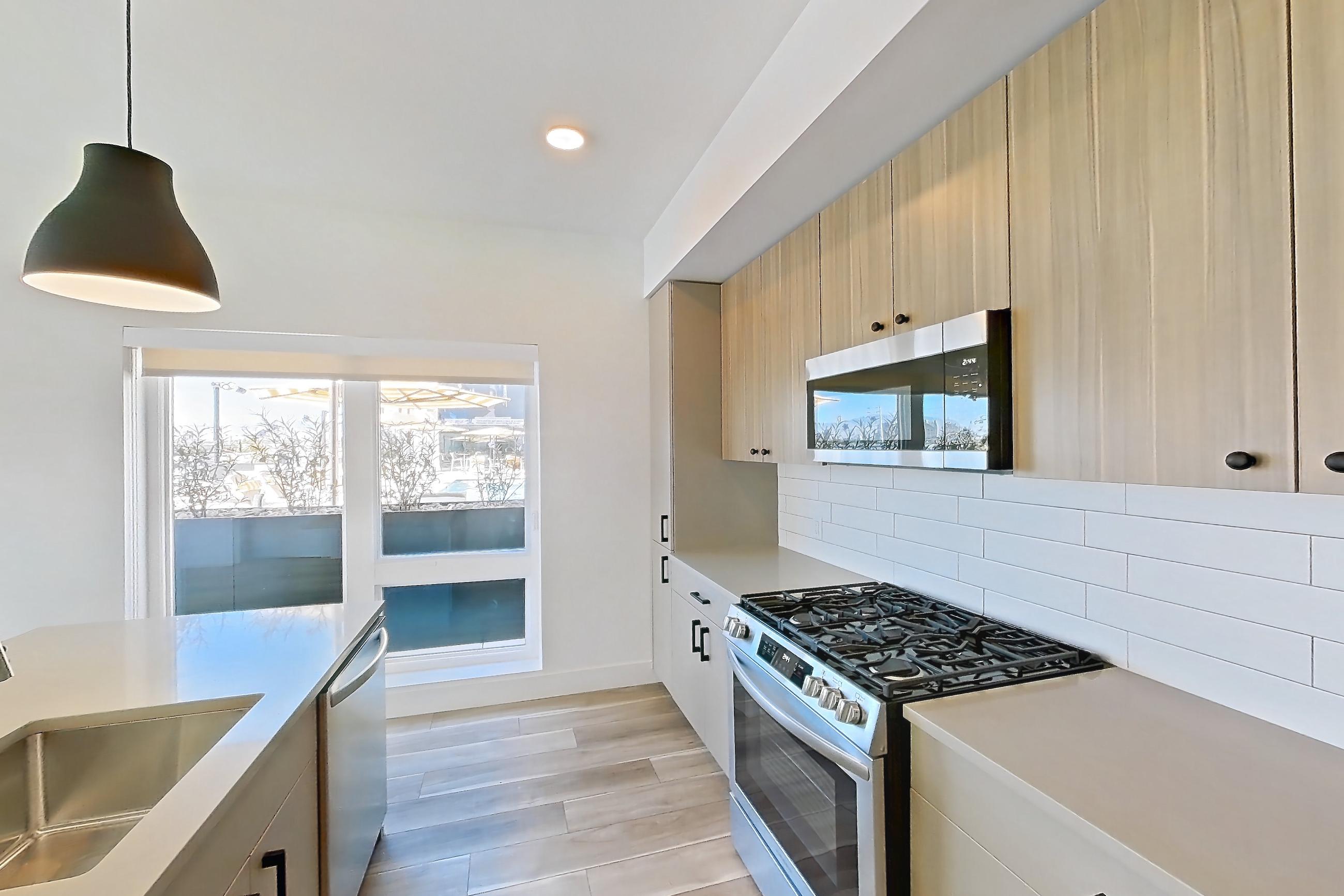 Kitchen with gas range, kitchen island, light countertops, light wood-finish flooring, oven/range, and stainless steel appliances, Apartment 333 at The Myles