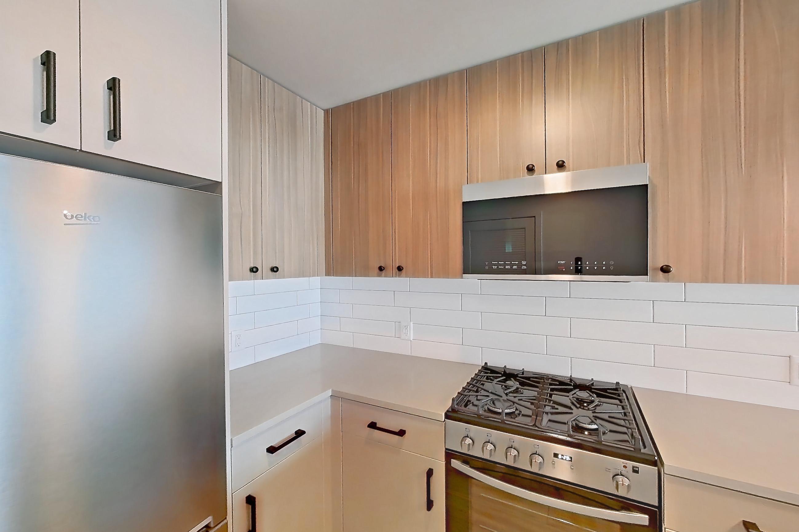 Kitchen with cooktop, gas range, light countertops, light wood-finish flooring, oven/range, refrigerator, and stainless steel appliances, Apartment 335 at The Myles