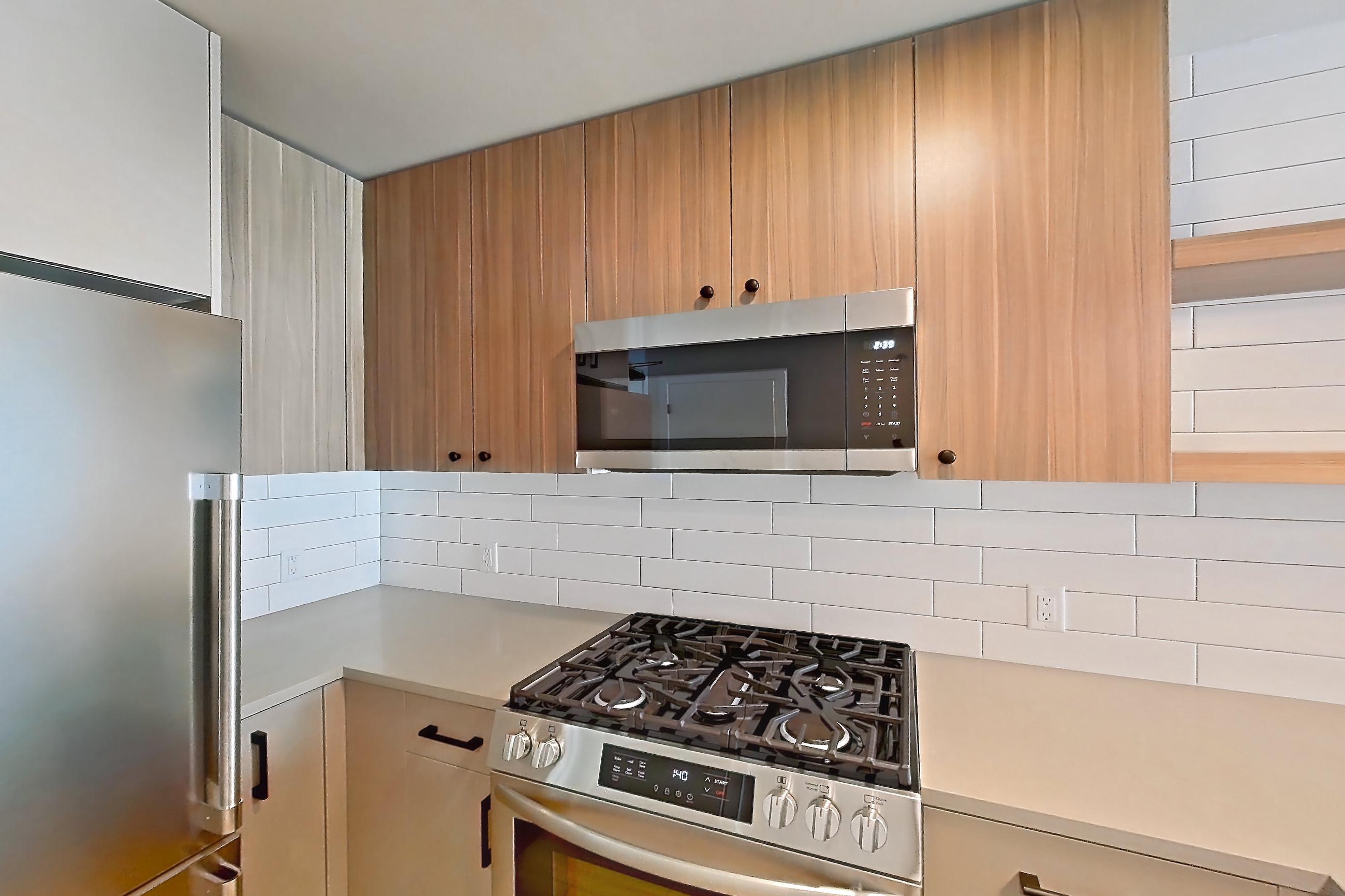 Kitchen with dishwasher, gas range, light countertops, light wood-finish flooring, oven/range, refrigerator, stainless steel appliances, and wood-look tile flooring, Apartment 337 at The Myles