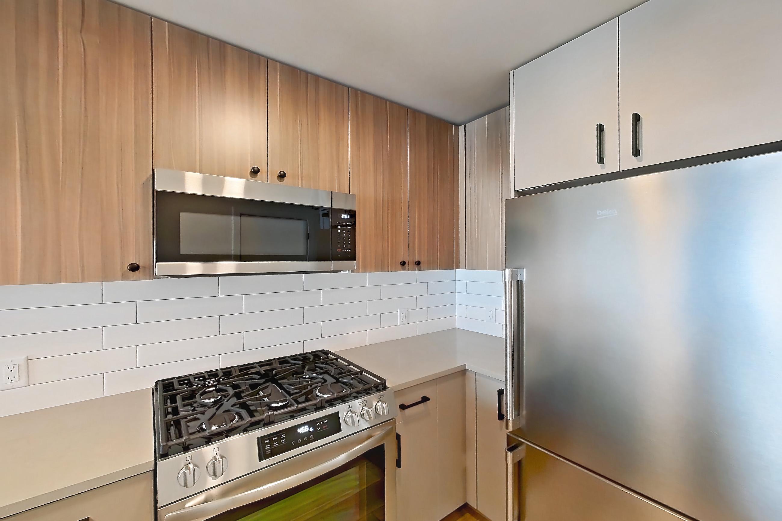 Kitchen with dishwasher, gas range, light countertops, light wood-finish flooring, microwave, oven/range, refrigerator, and stainless steel appliances, Apartment 339 at The Myles
