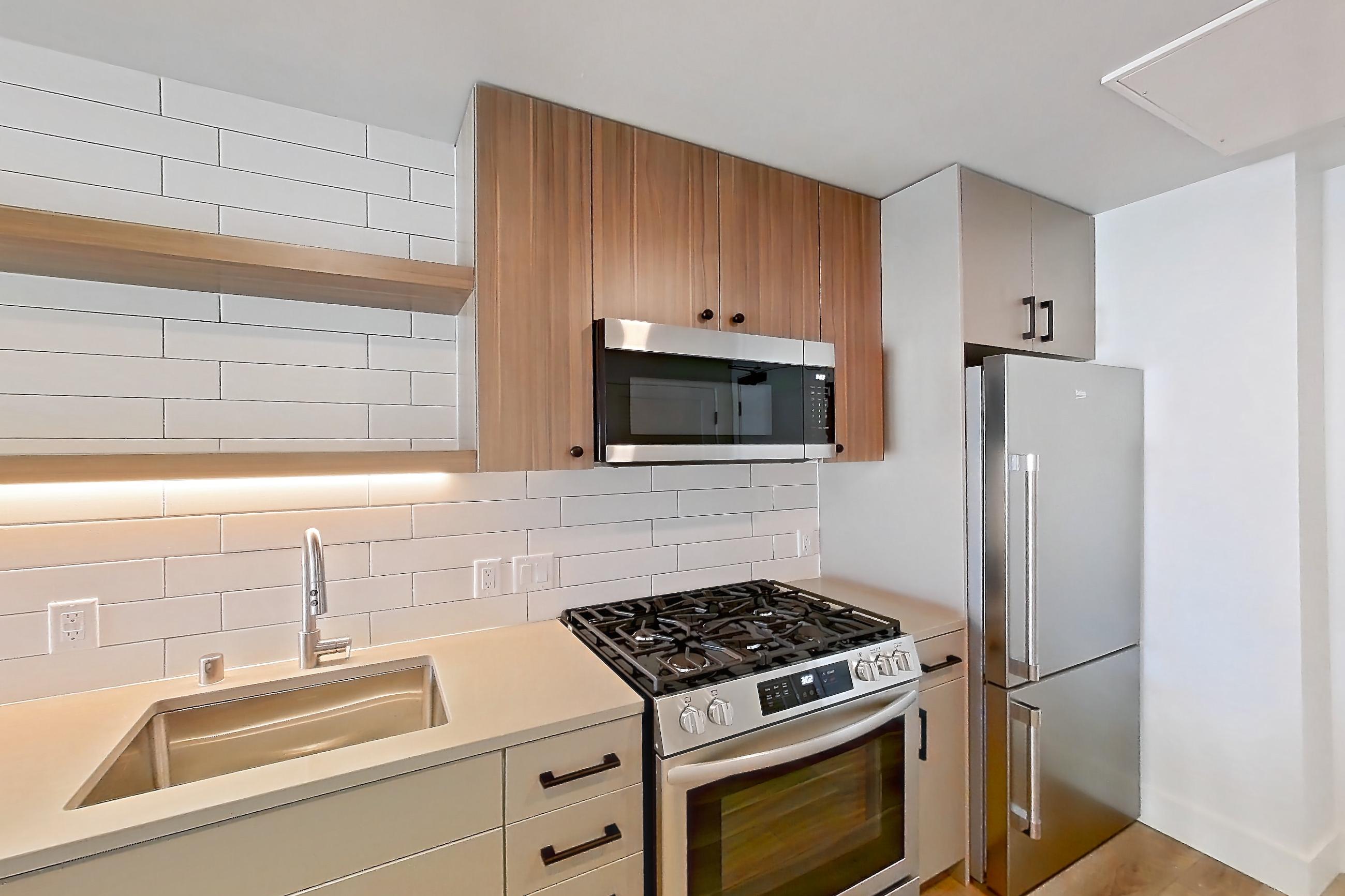 Kitchen with dishwasher, gas range, light countertops, light wood-finish flooring, microwave, oven/range, refrigerator, and stainless steel appliances, Apartment 341 at The Myles