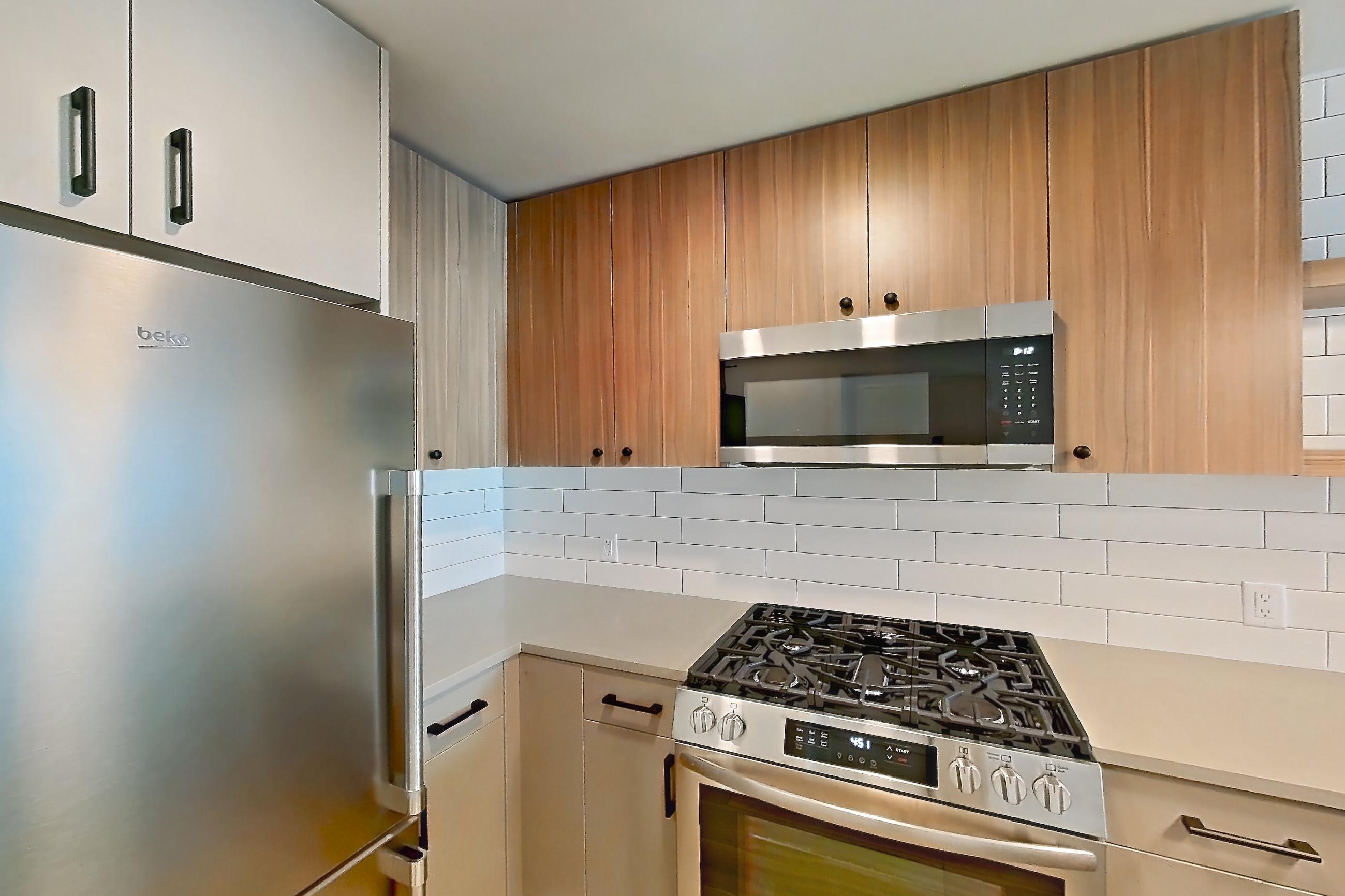 Kitchen with dishwasher, gas range, light countertops, light wood-finish flooring, oven/range, refrigerator, stainless steel appliances, and wood-look tile flooring, Apartment 347 at The Myles