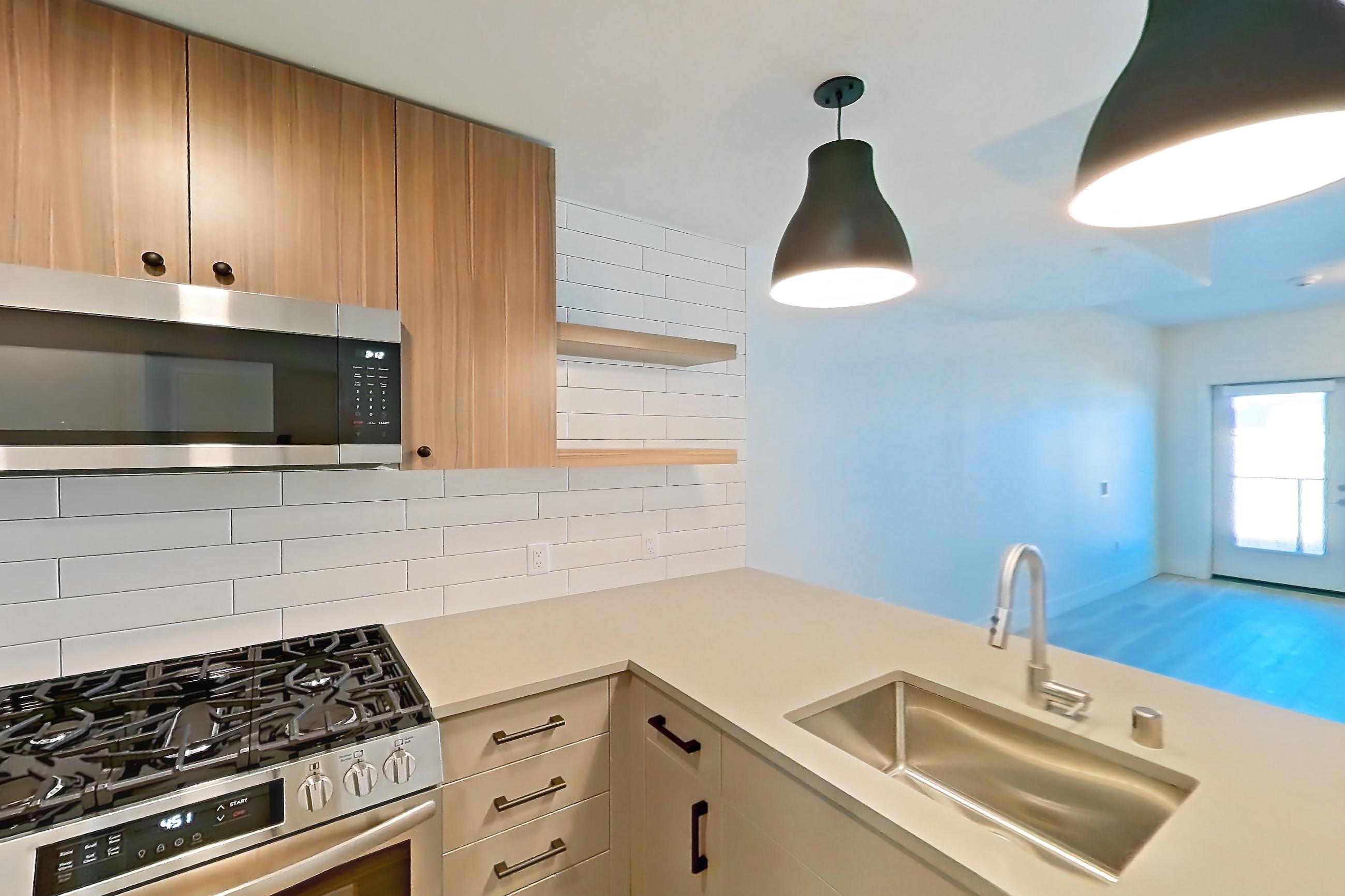 Kitchen with dishwasher, gas range, light countertops, light wood-finish flooring, oven/range, refrigerator, stainless steel appliances, and wood-look tile flooring, Apartment 347 at The Myles