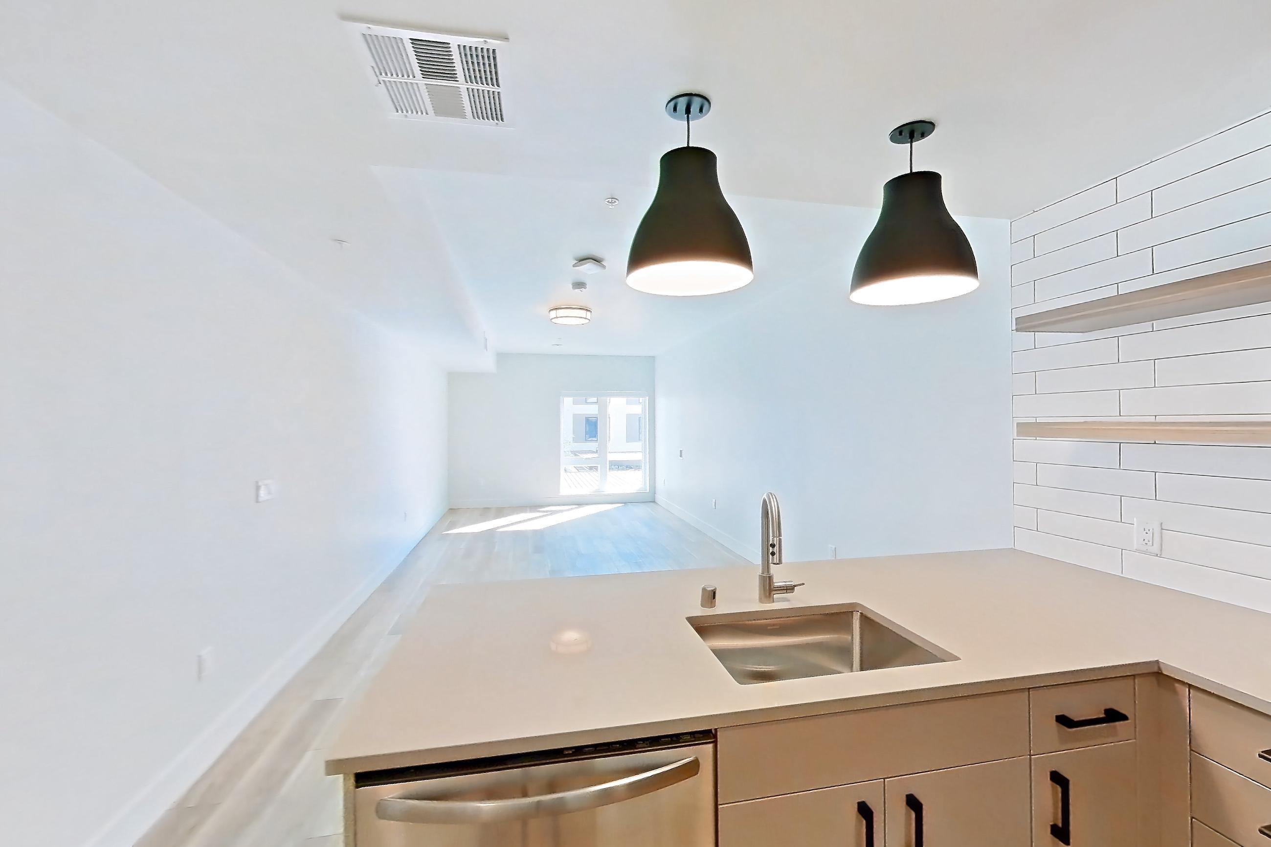 Kitchen with dishwasher, gas range, light countertops, light stone countertops, light wood-finish flooring, oven/range, refrigerator, stainless steel appliances, and wood-look tile flooring, Apartment 401 at The Myles