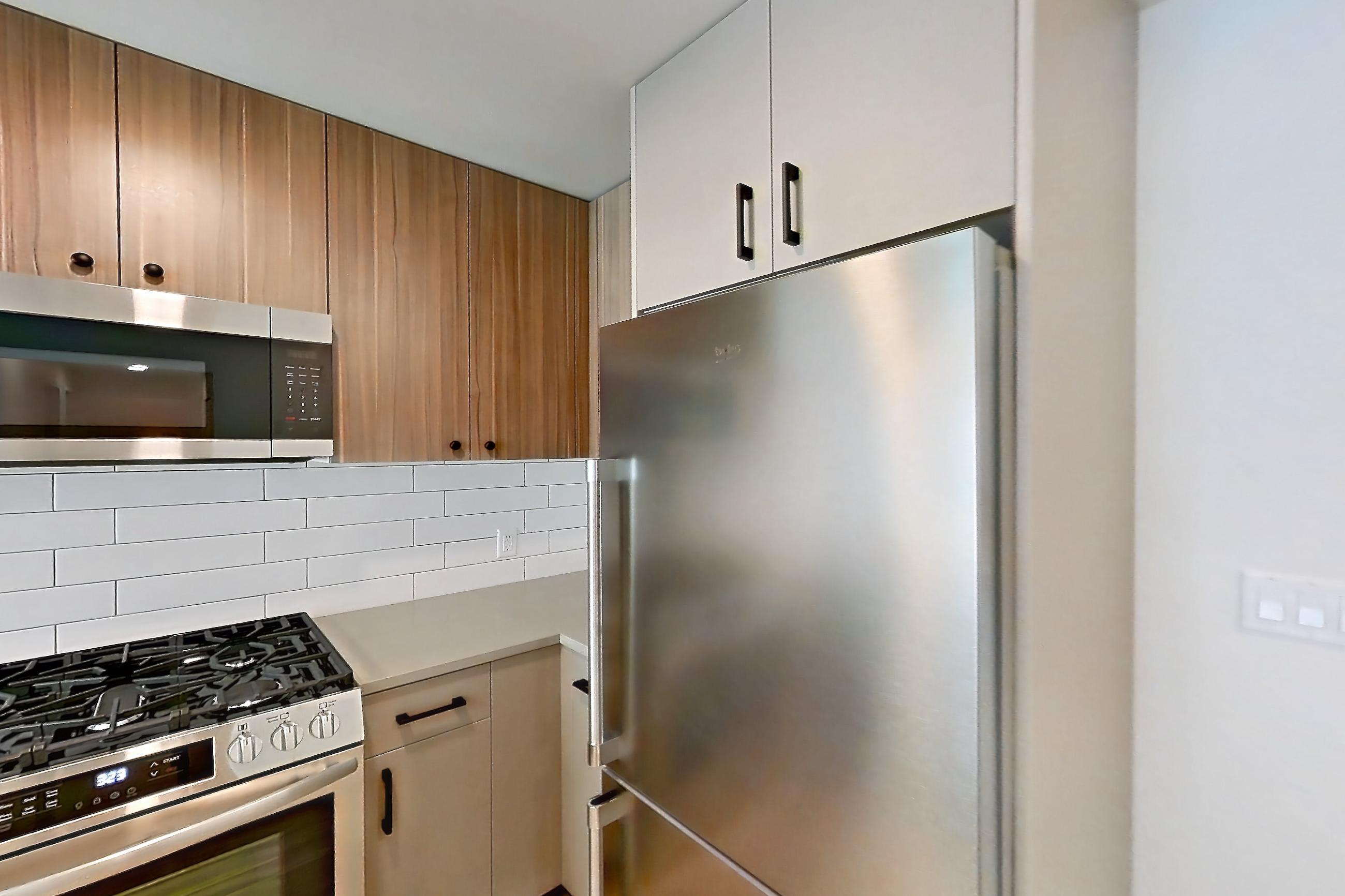 Kitchen with dishwasher, gas range, light countertops, light stone countertops, light wood-finish flooring, oven/range, refrigerator, stainless steel appliances, and wood-look tile flooring, Apartment 401 at The Myles