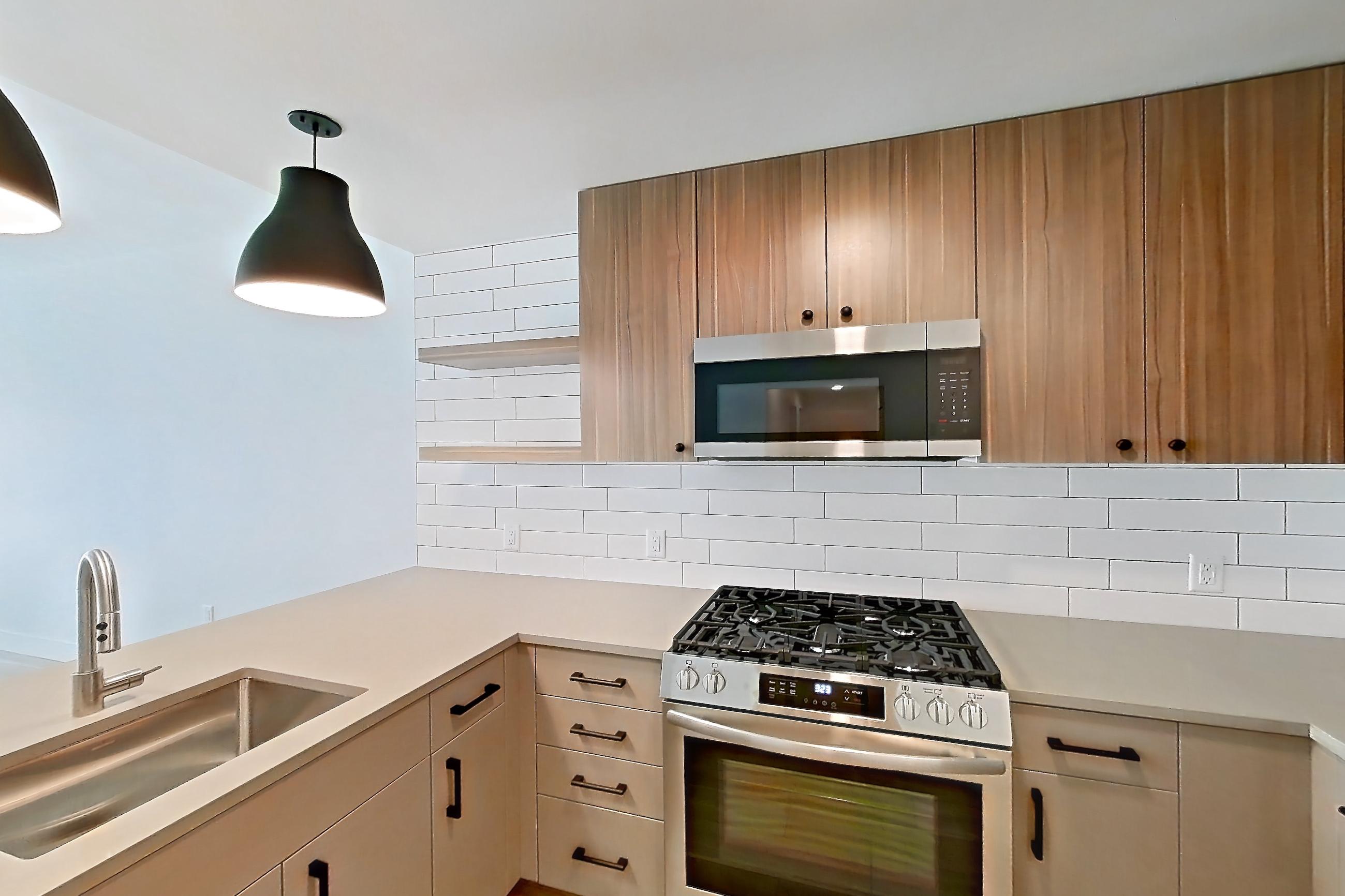 Kitchen with dishwasher, gas range, light countertops, light stone countertops, light wood-finish flooring, oven/range, refrigerator, stainless steel appliances, and wood-look tile flooring, Apartment 401 at The Myles