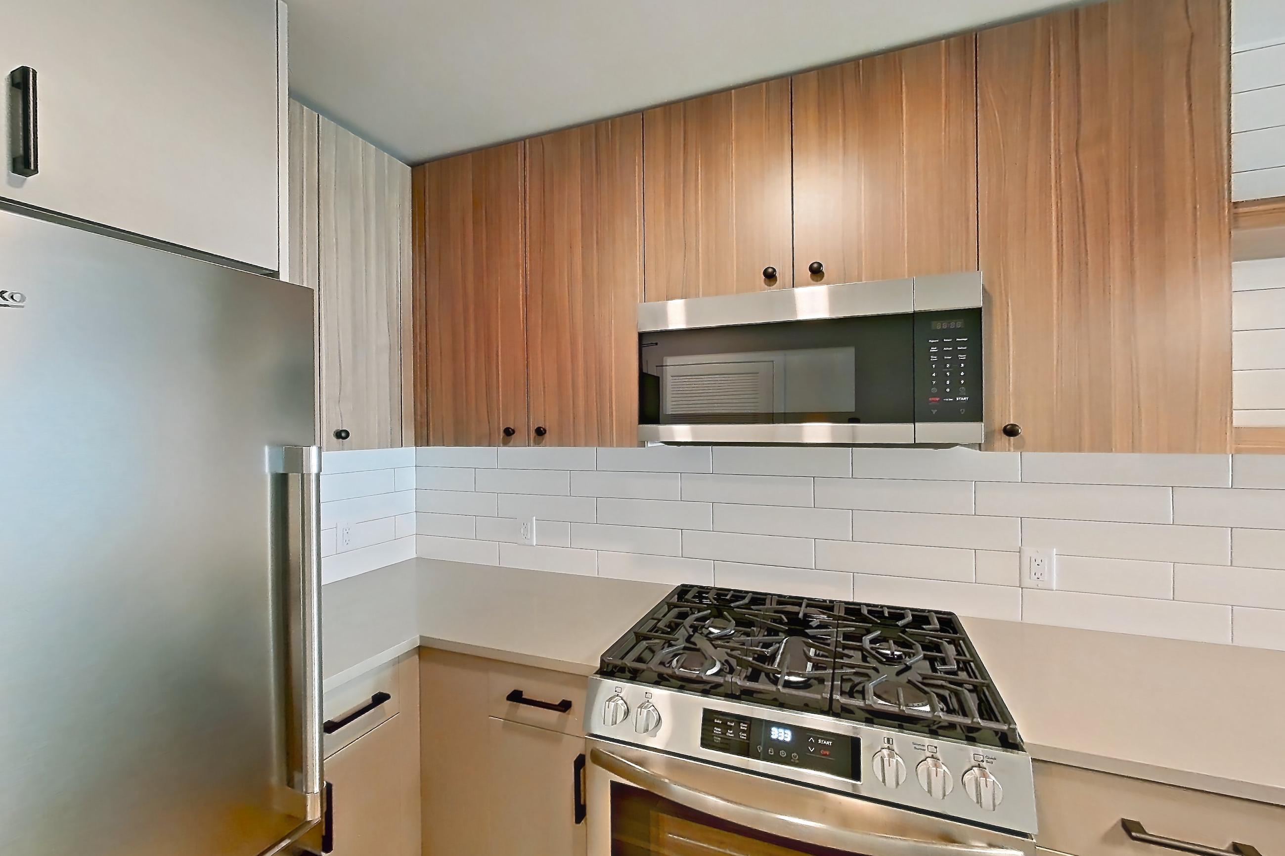 Kitchen with dishwasher, gas range, light countertops, light wood-finish flooring, oven/range, refrigerator, and stainless steel appliances, Apartment 402 at The Myles