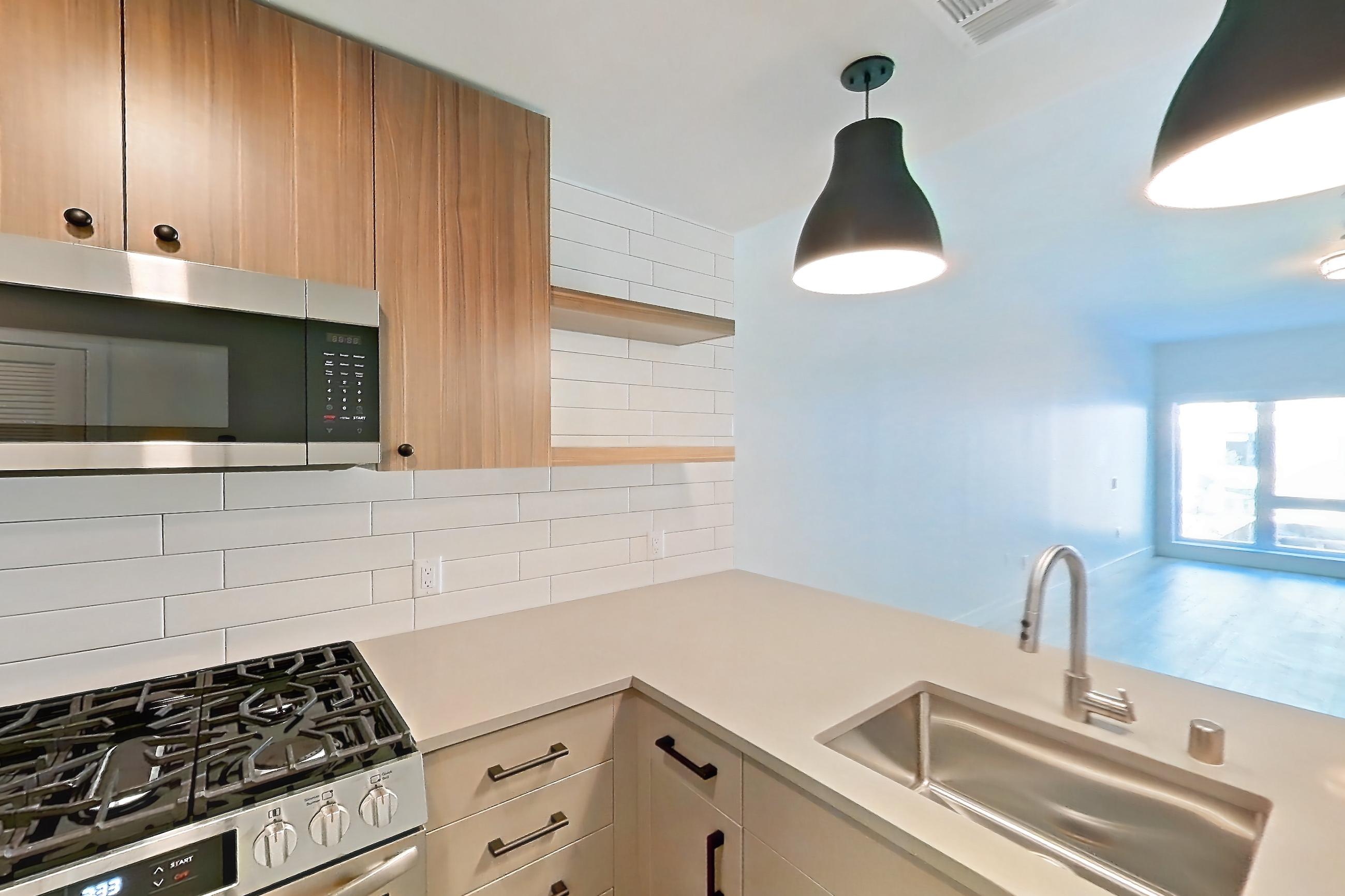 Kitchen with dishwasher, gas range, light countertops, light wood-finish flooring, oven/range, refrigerator, and stainless steel appliances, Apartment 402 at The Myles