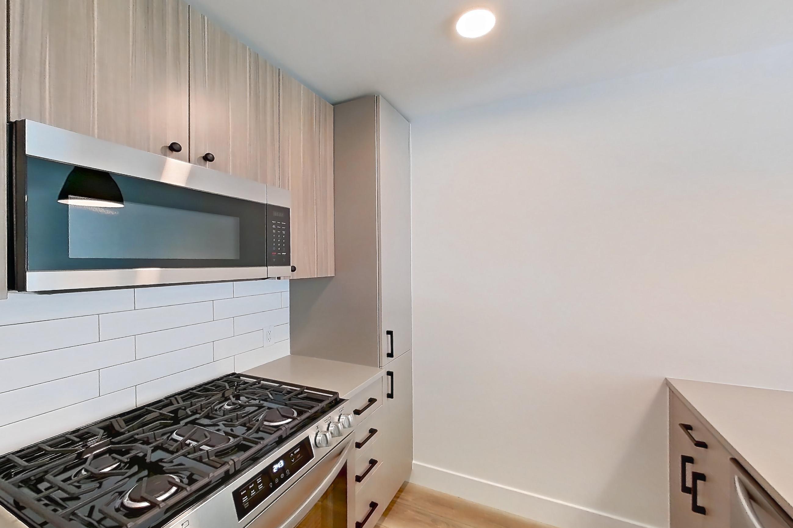 Kitchen with dishwasher, gas range, light countertops, light wood-finish flooring, oven/range, refrigerator, and stainless steel appliances, Apartment 403 at The Myles