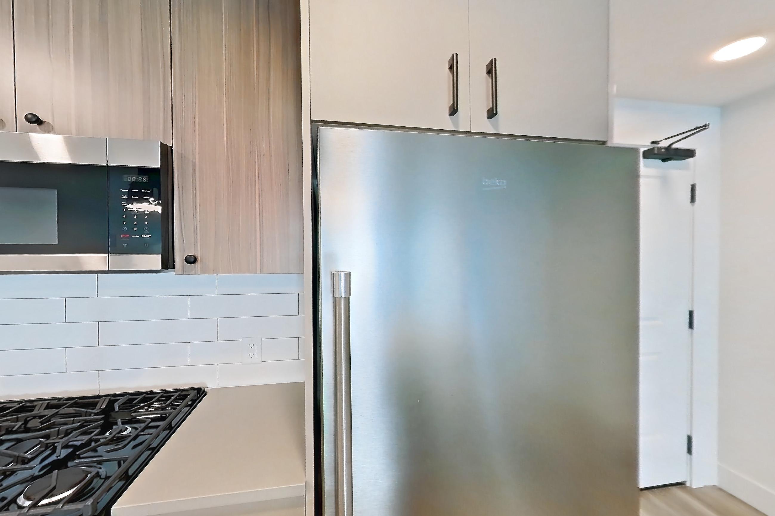 Kitchen with dishwasher, gas range, light countertops, light wood-finish flooring, microwave, oven/range, refrigerator, and stainless steel appliances, Apartment 404 at The Myles