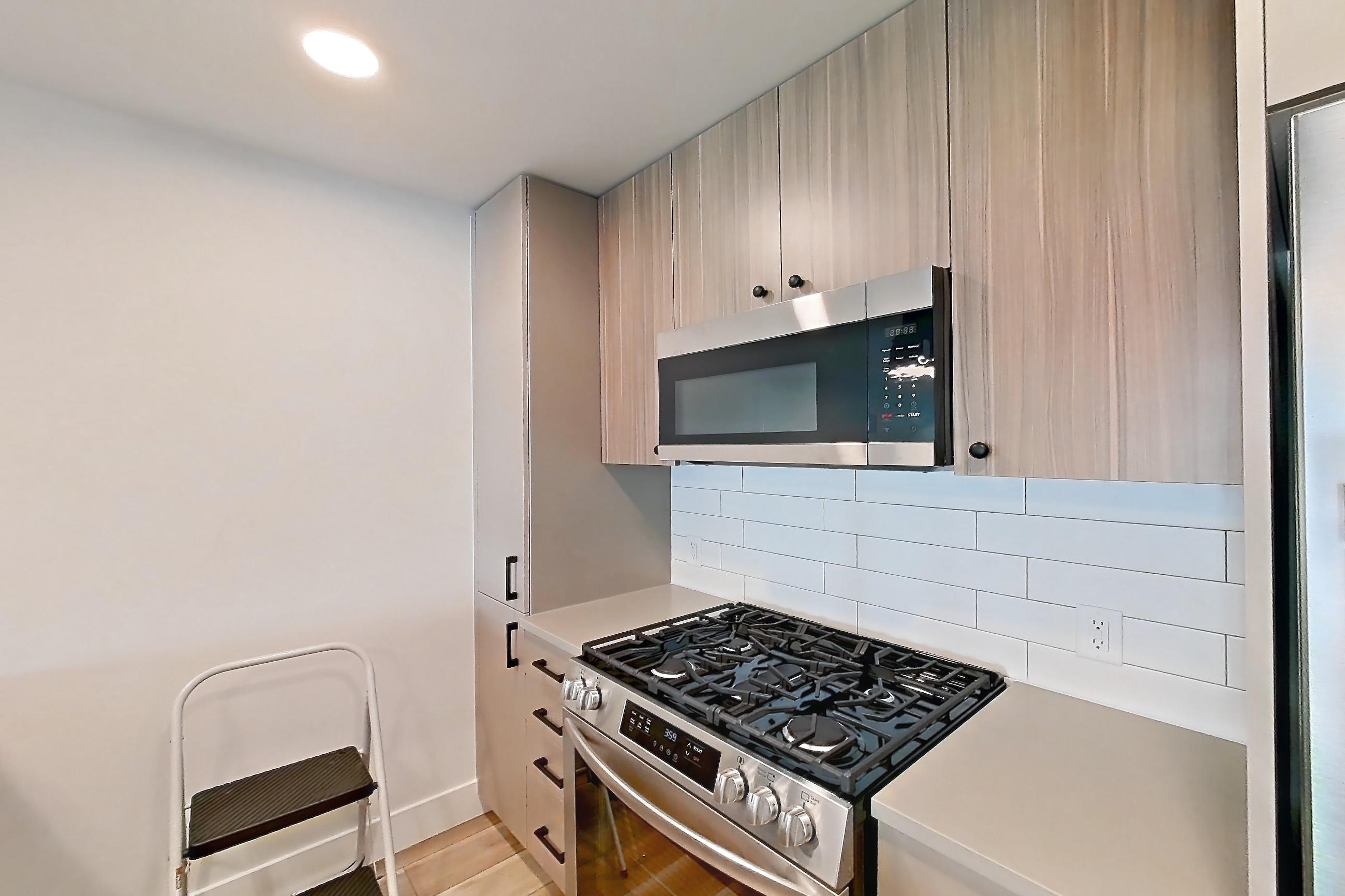 Kitchen with dishwasher, gas range, light countertops, light wood-finish flooring, microwave, oven/range, refrigerator, and stainless steel appliances, Apartment 404 at The Myles