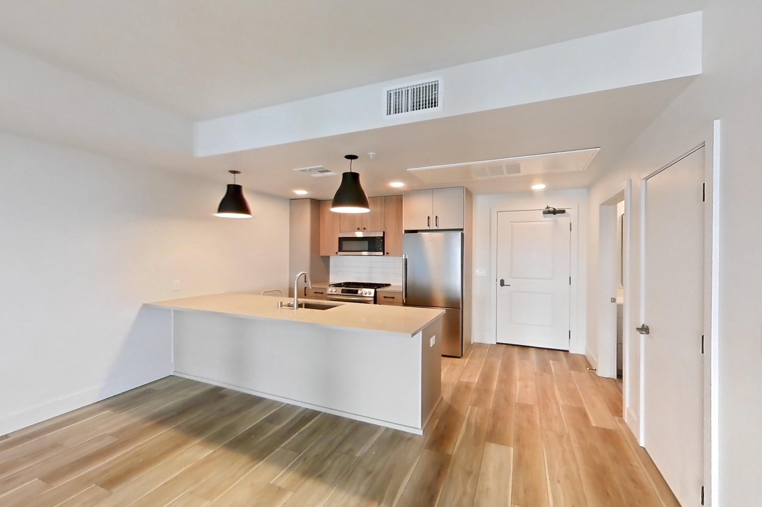 Living room with gas range, light countertops, light wood-finish flooring, oven/range, refrigerator, and stainless steel appliances, Apartment 404 at The Myles