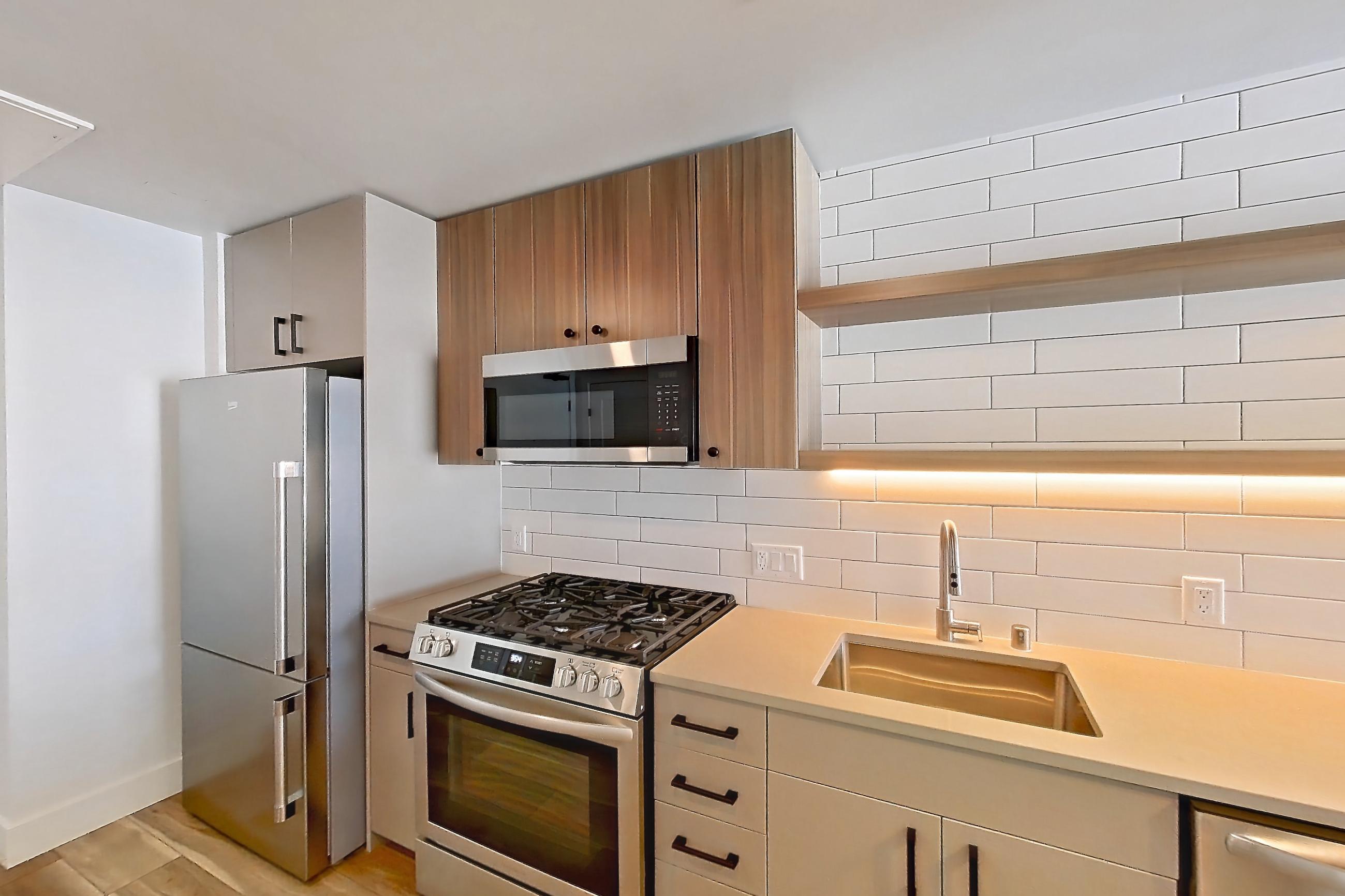Kitchen with dishwasher, gas range, light countertops, light wood-finish flooring, microwave, oven/range, refrigerator, and stainless steel appliances, Apartment 409 at The Myles