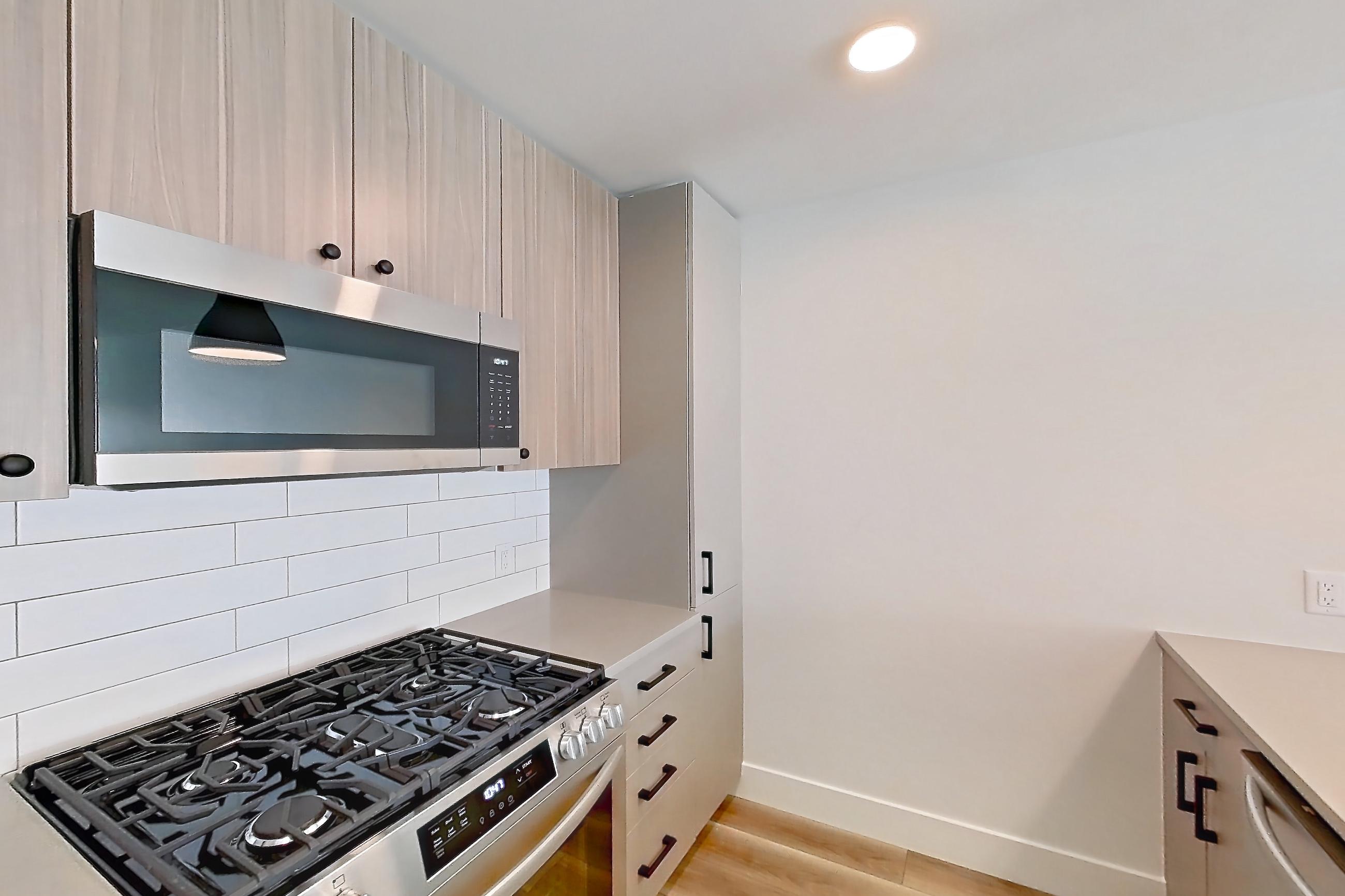 Kitchen with dishwasher, gas range, light countertops, light wood-finish flooring, oven/range, refrigerator, and stainless steel appliances, Apartment 411 at The Myles