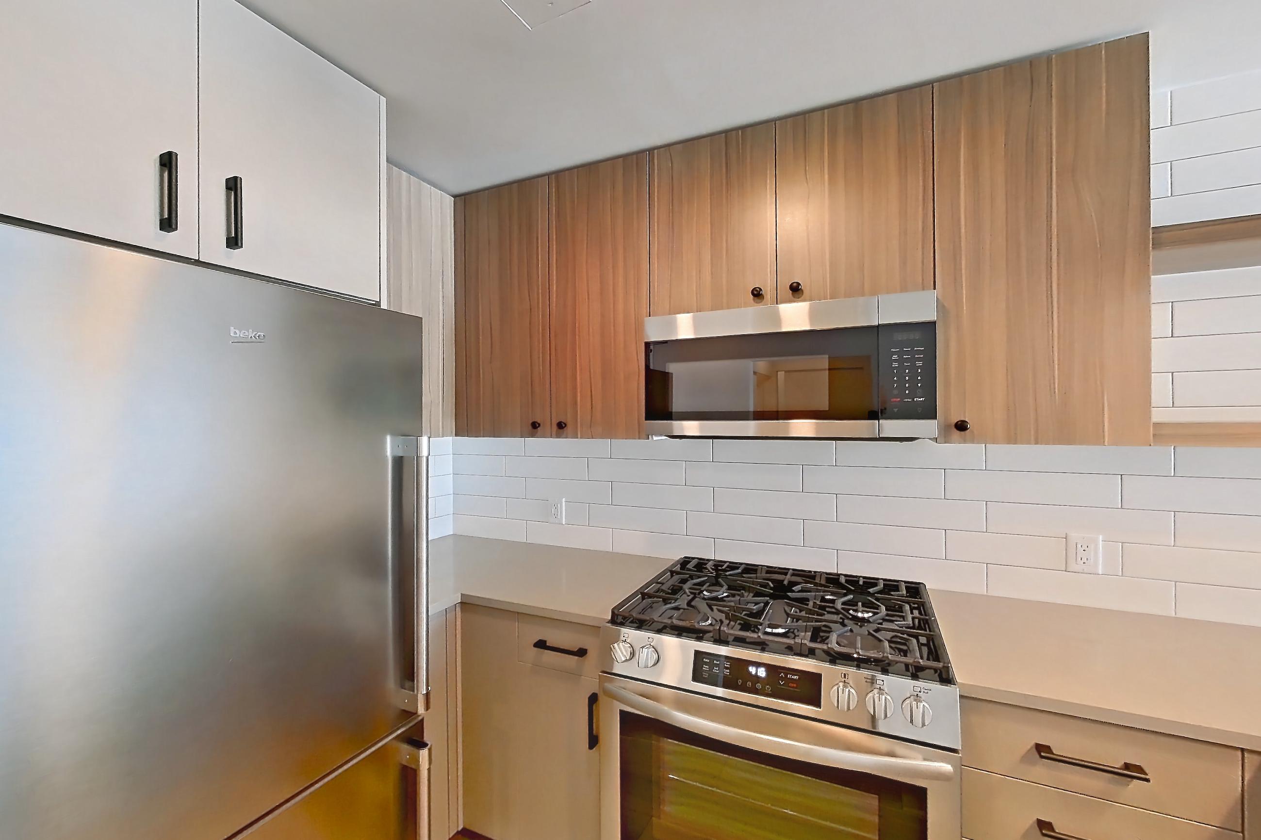 Kitchen with dishwasher, gas range, light countertops, light stone countertops, light wood-finish flooring, oven/range, refrigerator, and stainless steel appliances, Apartment 412 at The Myles