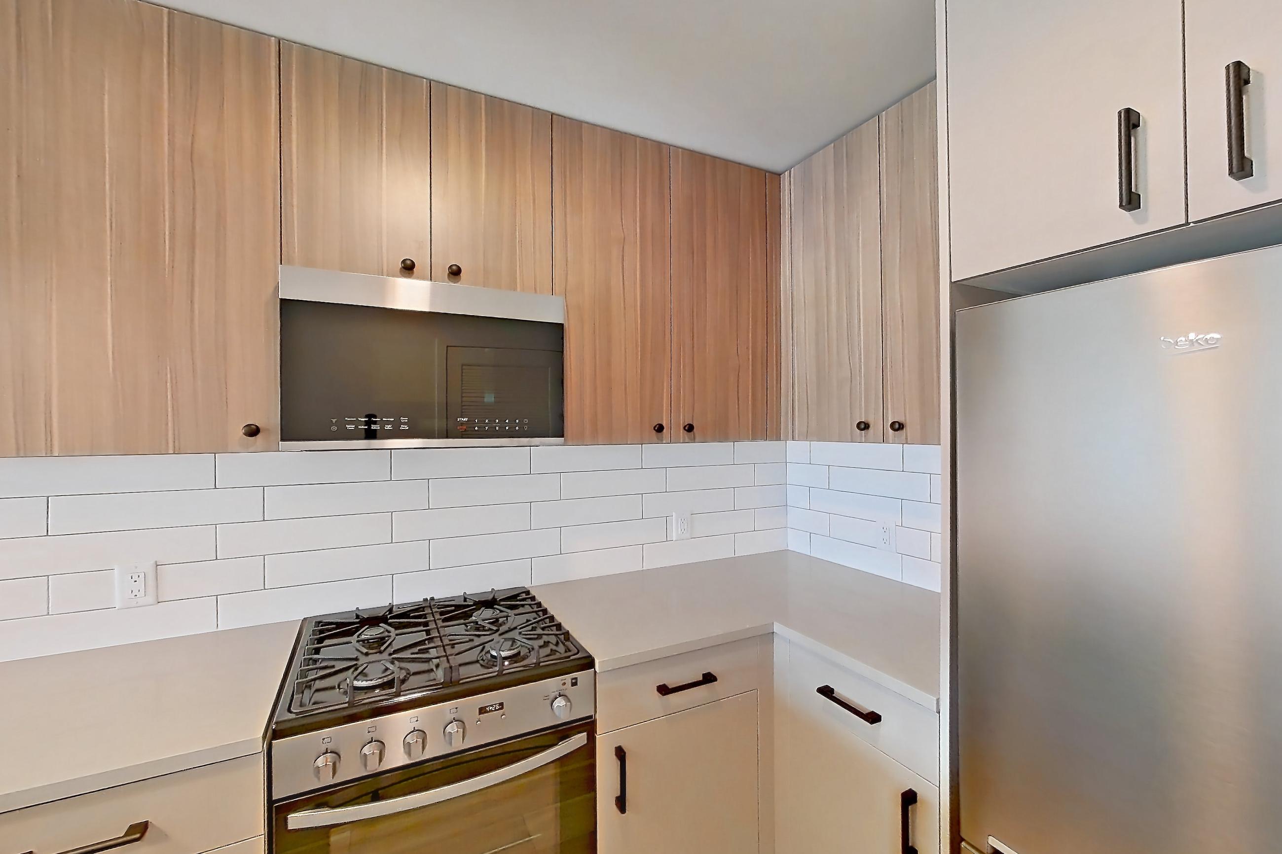 Kitchen with gas range, light countertops, light stone countertops, light wood-finish flooring, oven/range, refrigerator, stainless steel appliances, and wood-look tile flooring, Apartment 413 at The Myles