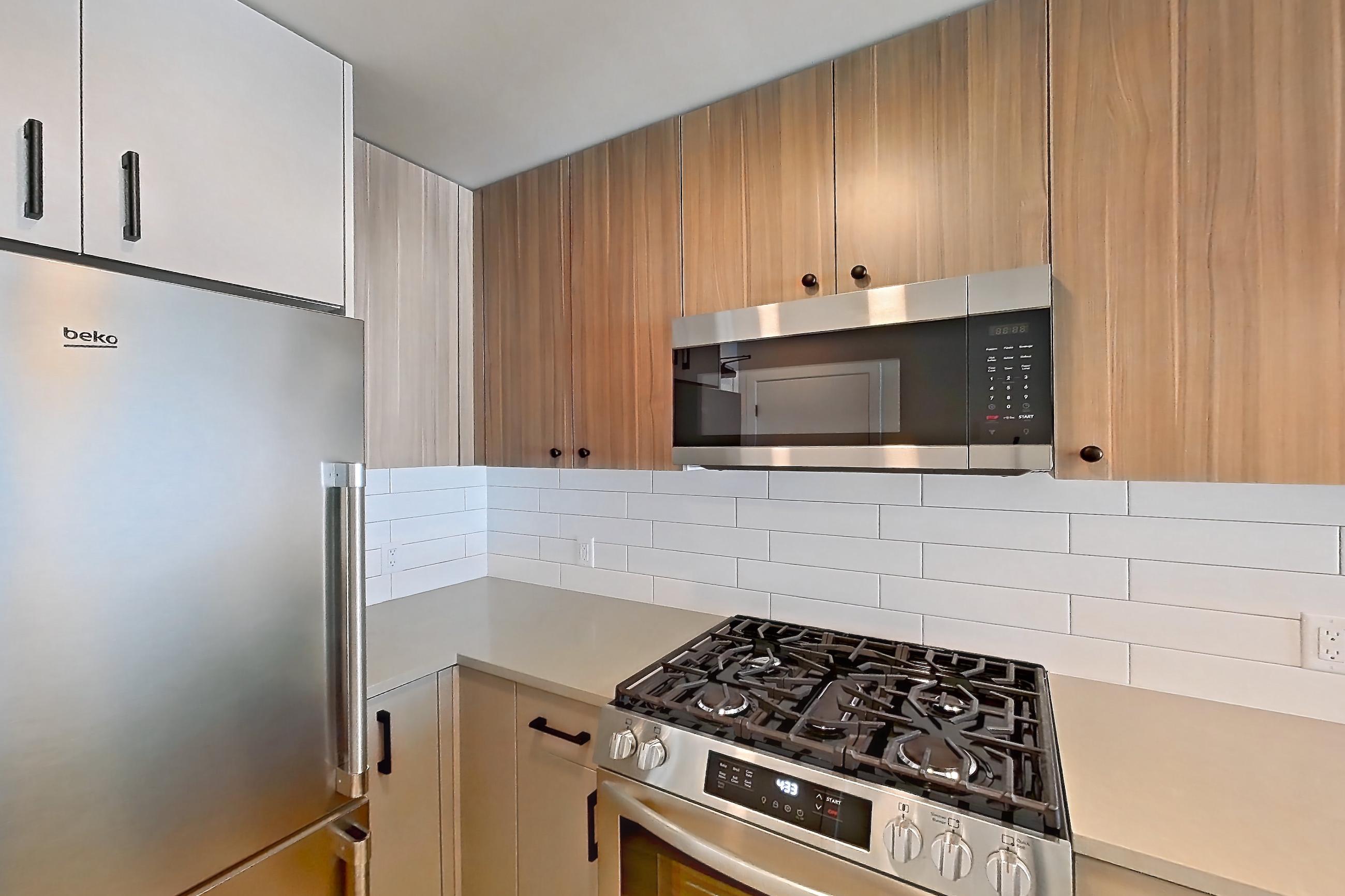 Kitchen with gas range, light countertops, light wood-finish flooring, microwave, oven/range, refrigerator, and stainless steel appliances, Apartment 414 at The Myles
