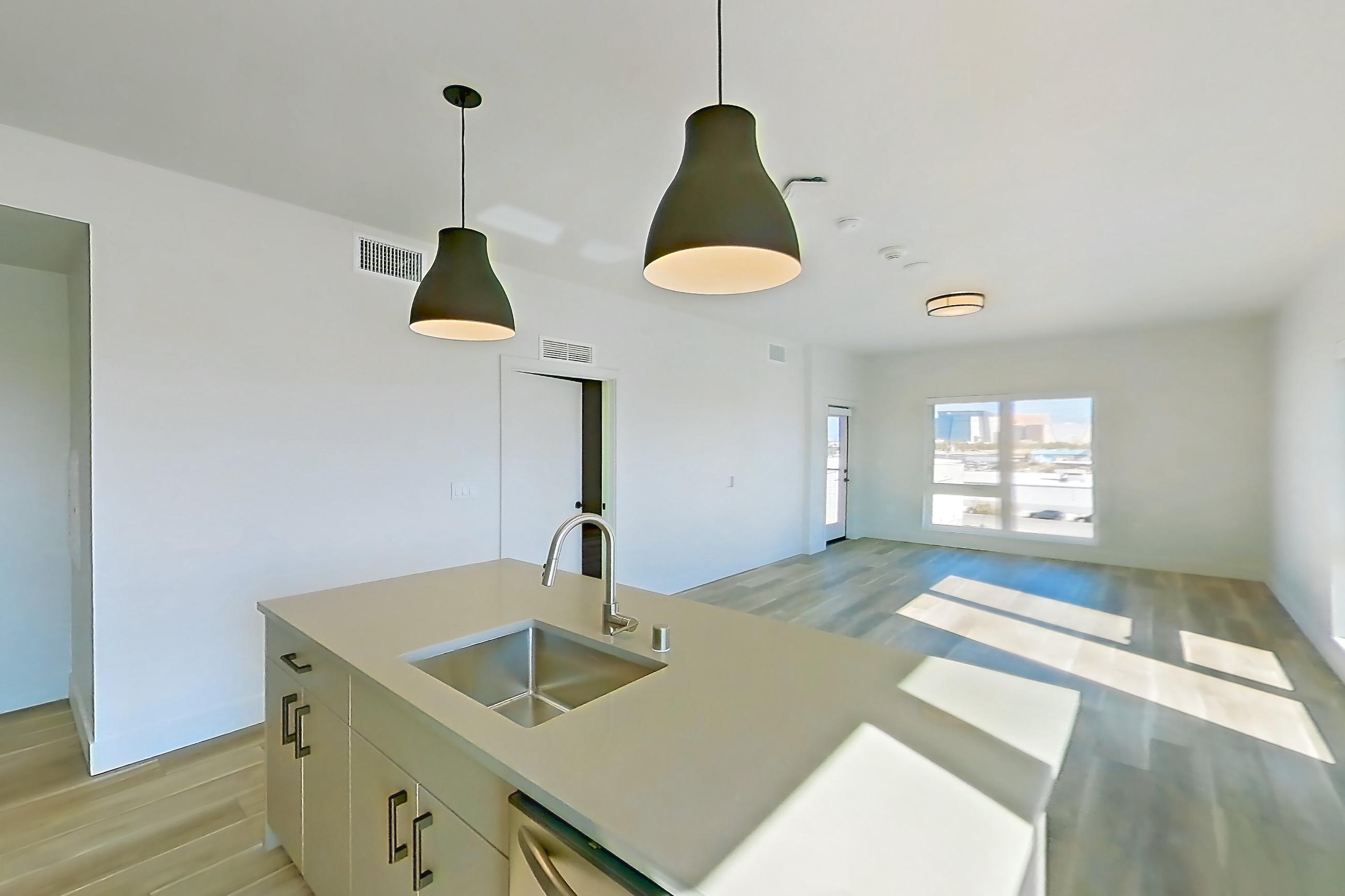 Kitchen with dishwasher, gas range, kitchen island, light countertops, light stone countertops, light wood-finish flooring, oven/range, refrigerator, and stainless steel appliances, Apartment 424 at The Myles