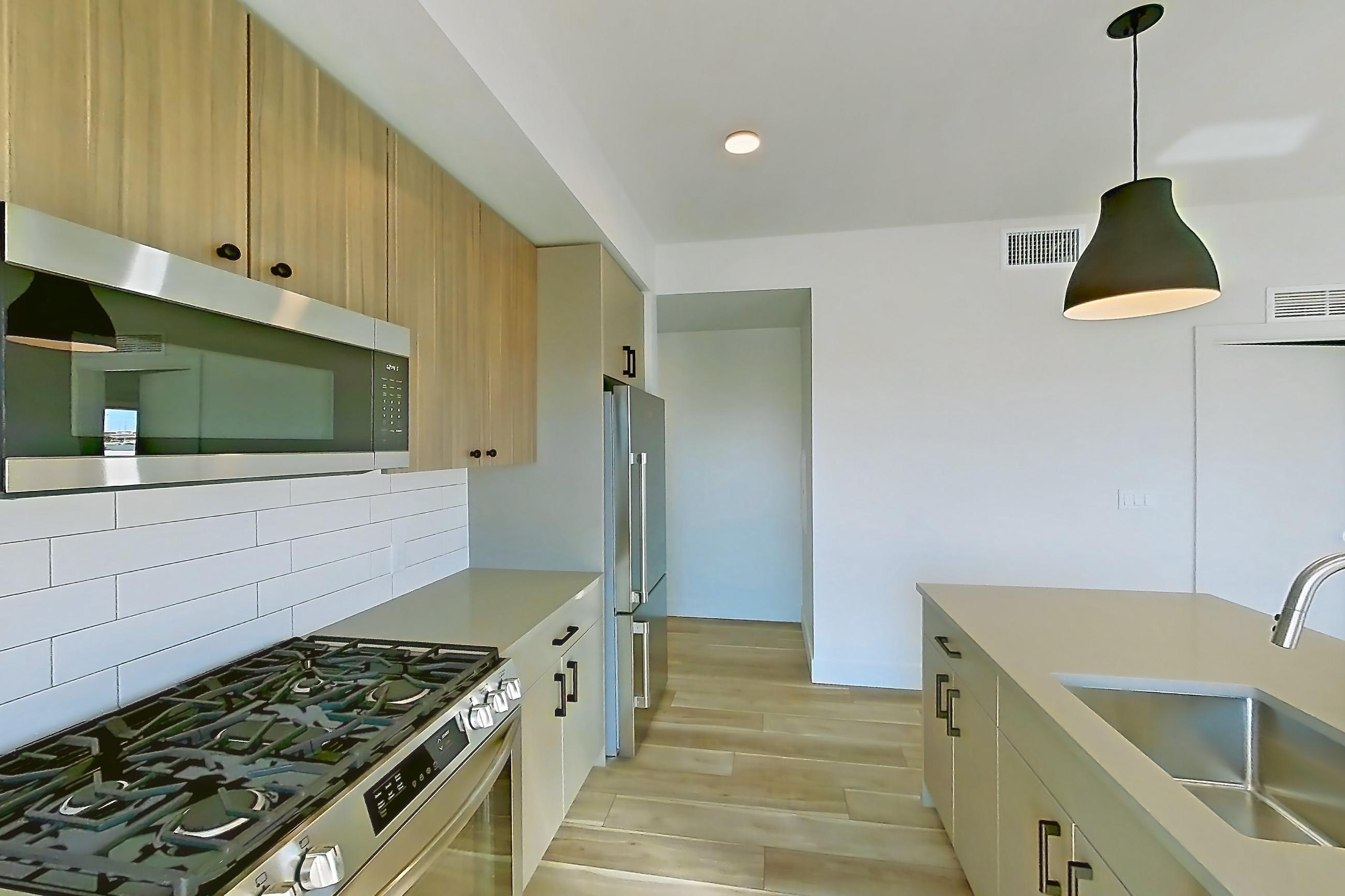 Kitchen with dishwasher, gas range, kitchen island, light countertops, light stone countertops, light wood-finish flooring, oven/range, refrigerator, and stainless steel appliances, Apartment 424 at The Myles