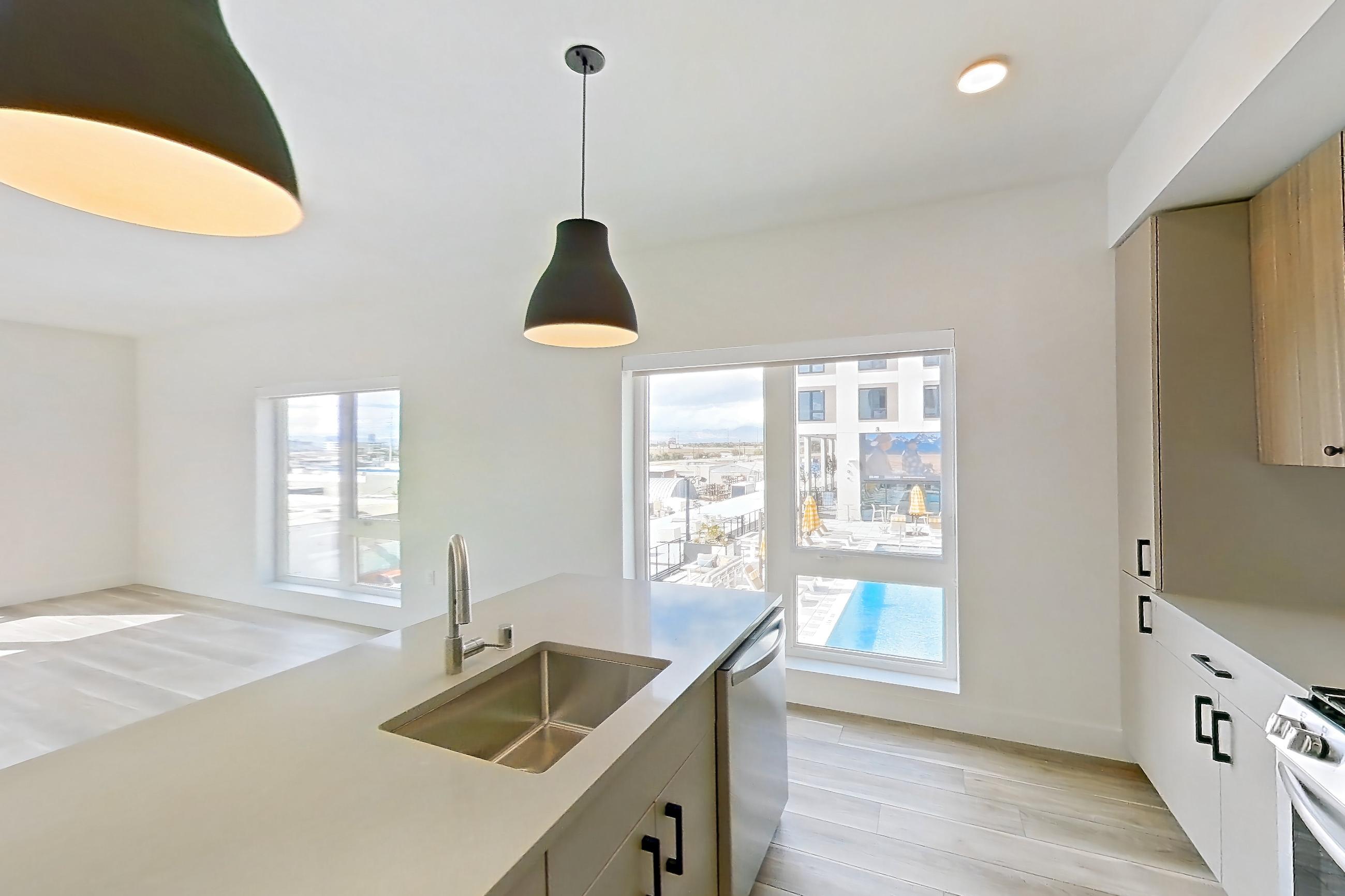 Kitchen with dishwasher, gas range, kitchen island, light countertops, light stone countertops, light wood-finish flooring, microwave, oven/range, and stainless steel appliances, Apartment 433 at The Myles