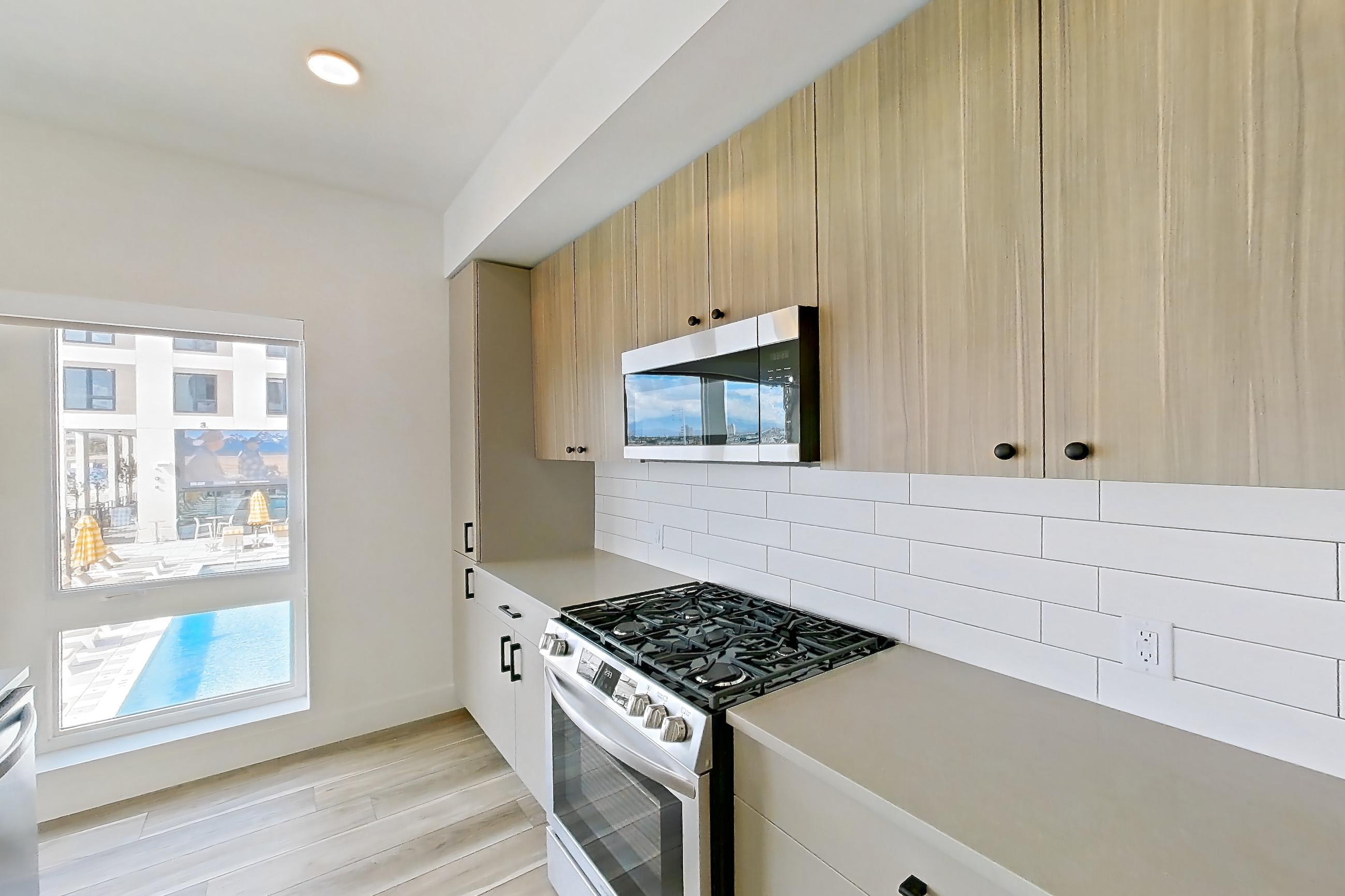 Kitchen with dishwasher, gas range, kitchen island, light countertops, light stone countertops, light wood-finish flooring, microwave, oven/range, and stainless steel appliances, Apartment 433 at The Myles