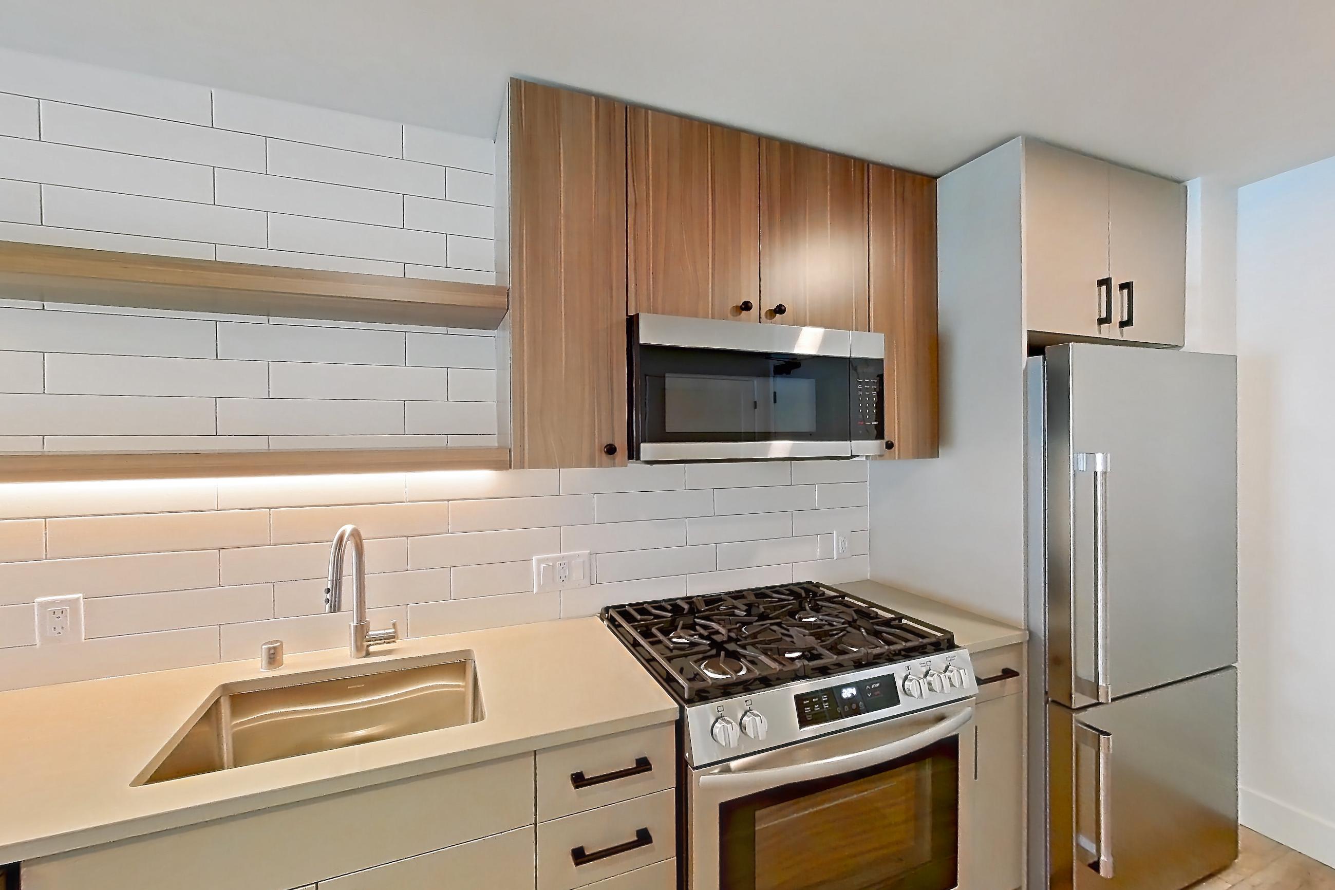 Kitchen with dishwasher, gas range, light countertops, light wood-finish flooring, microwave, oven/range, refrigerator, and stainless steel appliances, Apartment 434 at The Myles