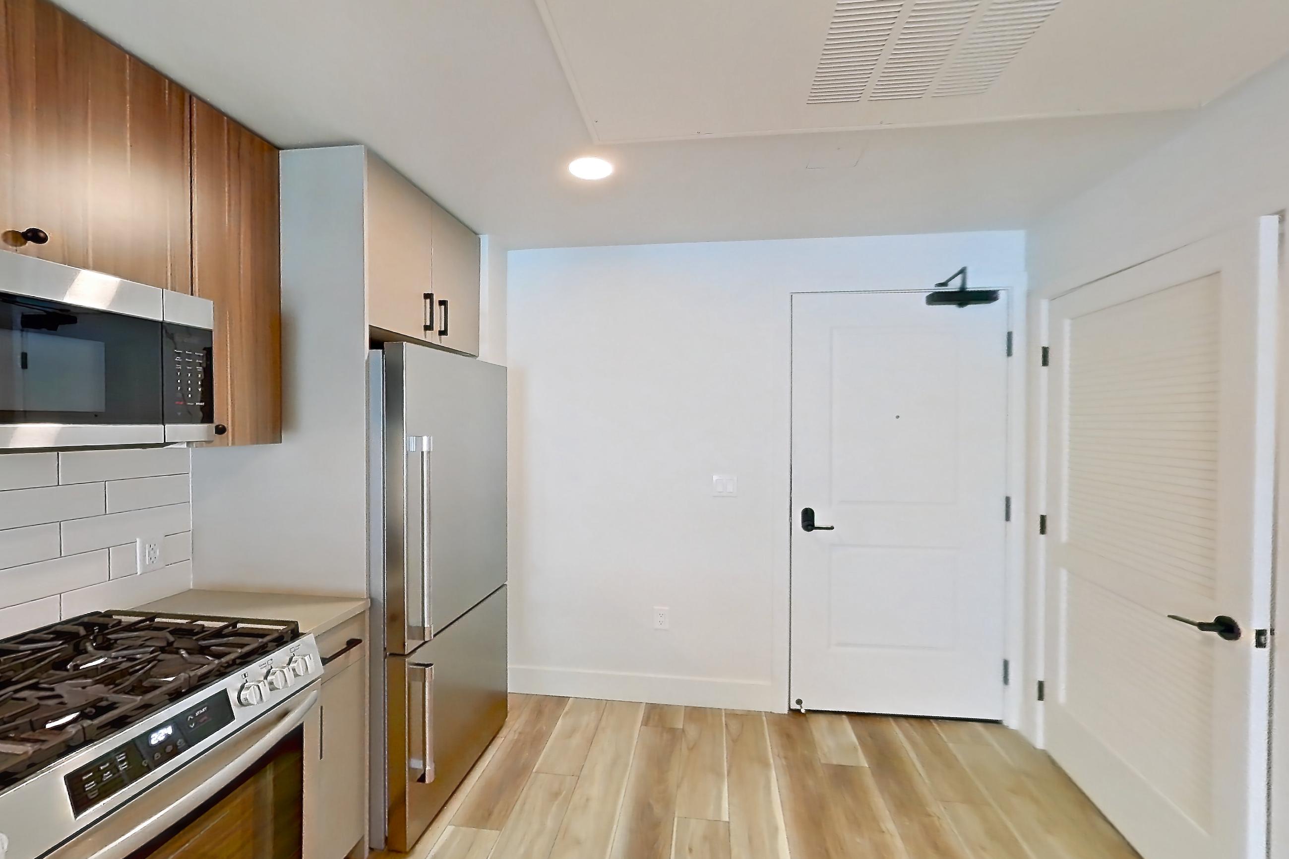 Kitchen with dishwasher, gas range, light countertops, light wood-finish flooring, microwave, oven/range, refrigerator, and stainless steel appliances, Apartment 434 at The Myles