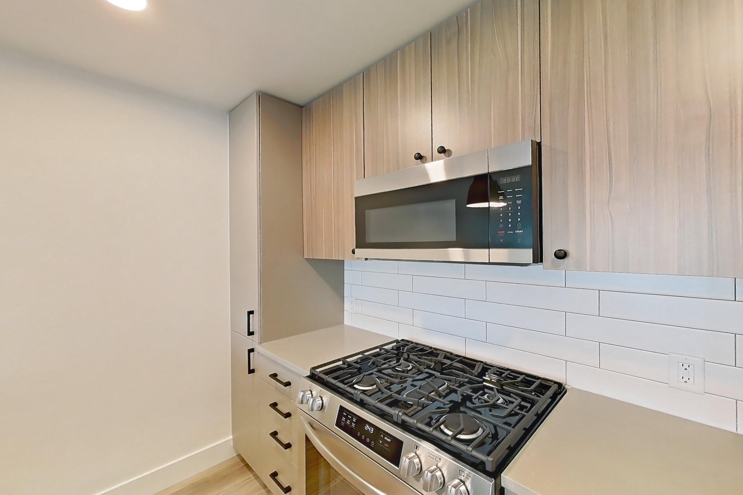 Kitchen with dishwasher, gas range, light countertops, light wood-finish flooring, oven/range, refrigerator, and stainless steel appliances, Apartment 436 at The Myles