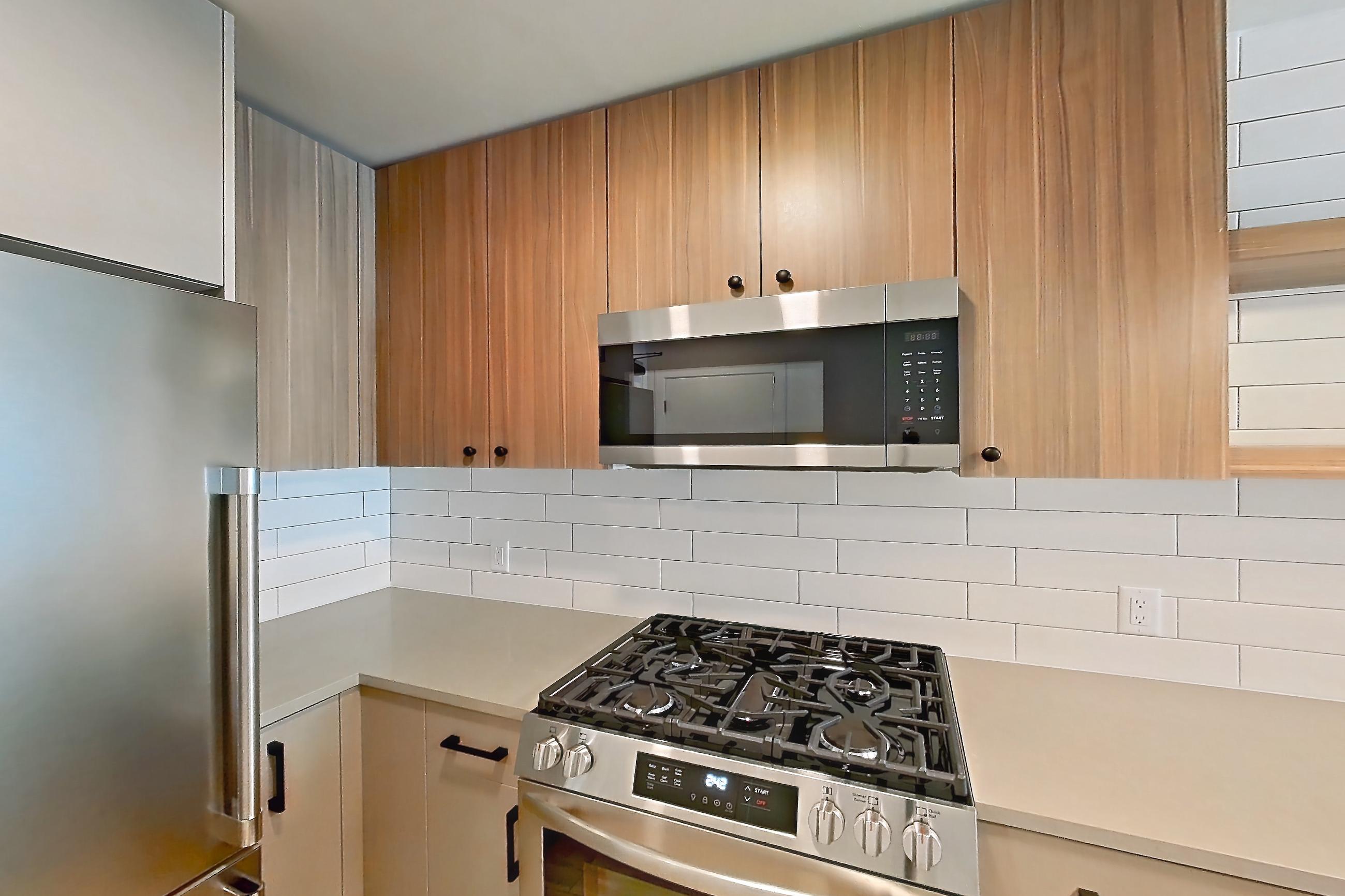 Kitchen with dishwasher, gas range, light countertops, light wood-finish flooring, microwave, oven/range, refrigerator, and stainless steel appliances, Apartment 437 at The Myles