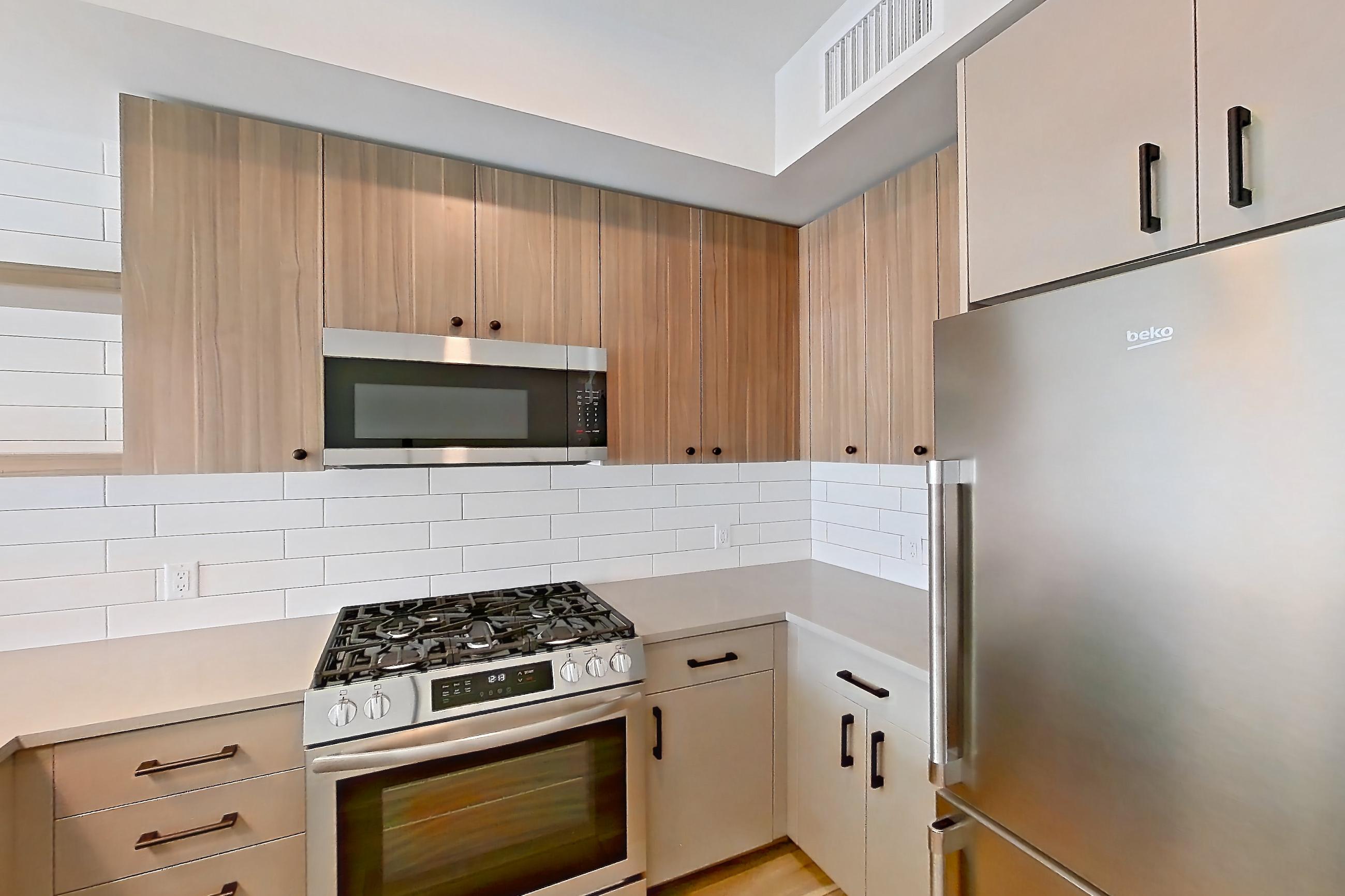 Kitchen with dishwasher, gas range, light countertops, light wood-finish flooring, microwave, oven/range, refrigerator, and stainless steel appliances, Apartment 440 at The Myles