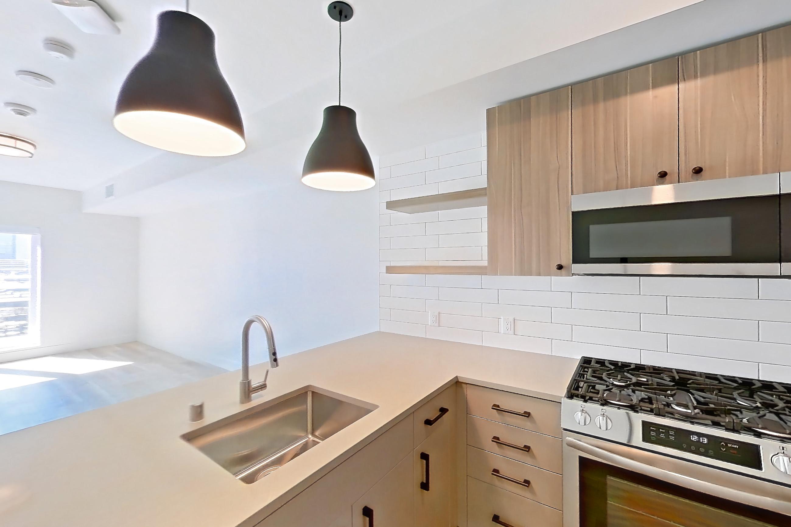 Kitchen with dishwasher, gas range, light countertops, light wood-finish flooring, microwave, oven/range, refrigerator, and stainless steel appliances, Apartment 440 at The Myles