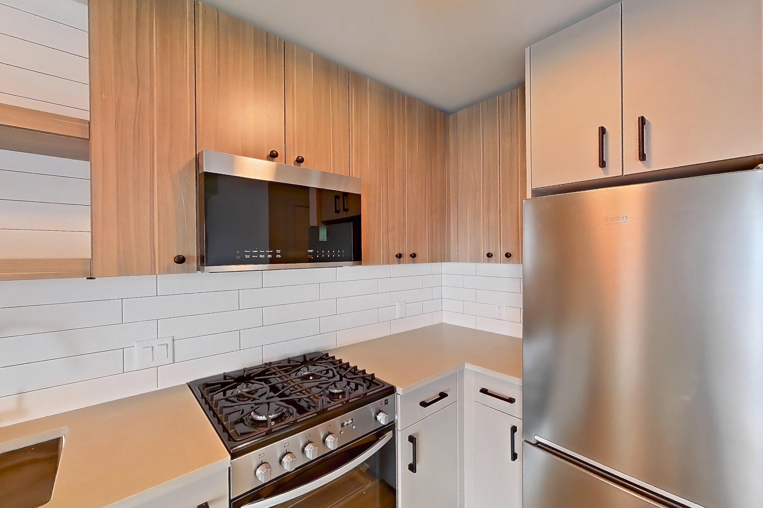 Kitchen with dishwasher, gas range, light countertops, light wood-finish flooring, oven/range, refrigerator, and stainless steel appliances, Apartment 443 at The Myles
