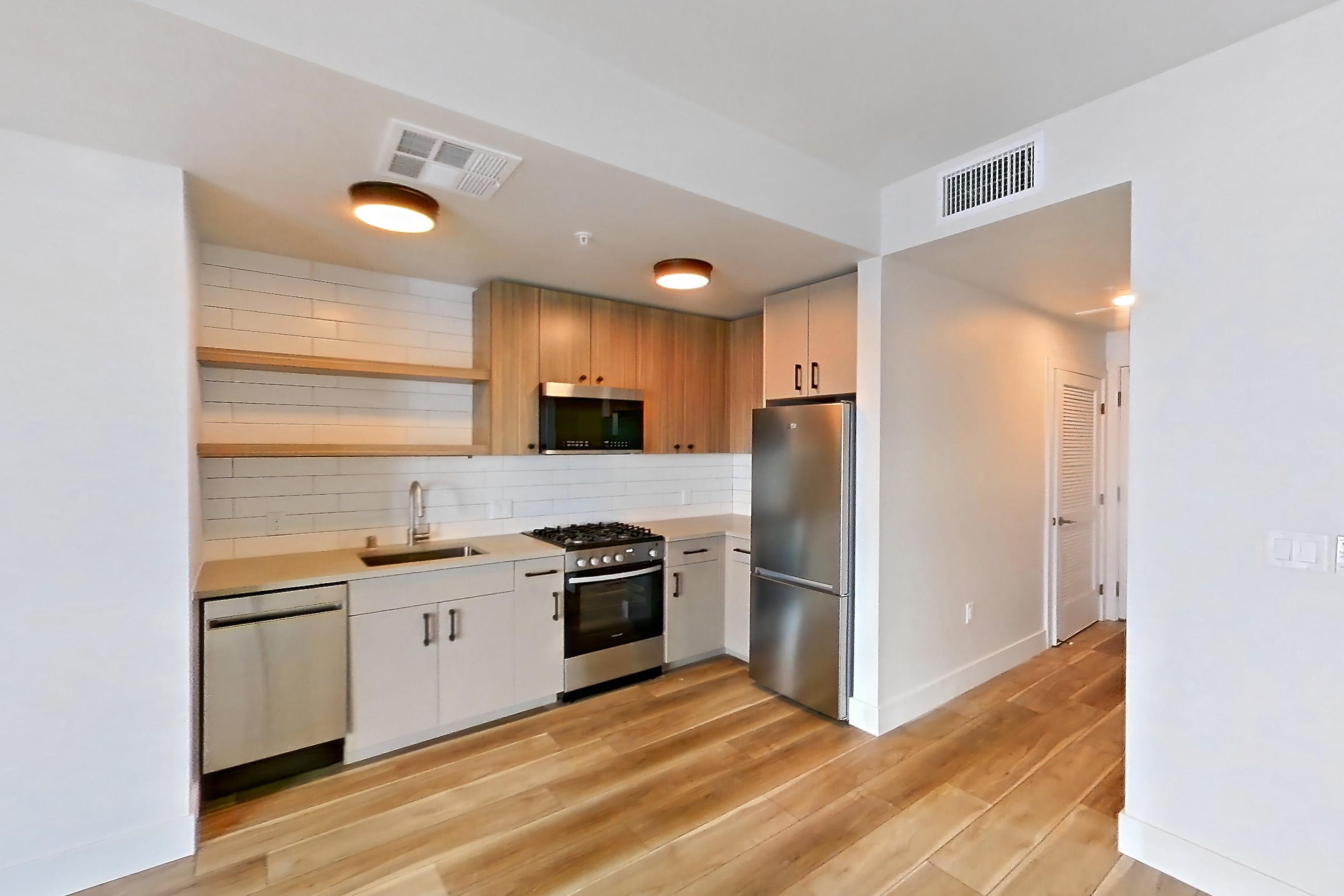 Living space with dishwasher, gas range, light countertops, light wood-finish flooring, oven/range, refrigerator, and stainless steel appliances, Apartment 443 at The Myles