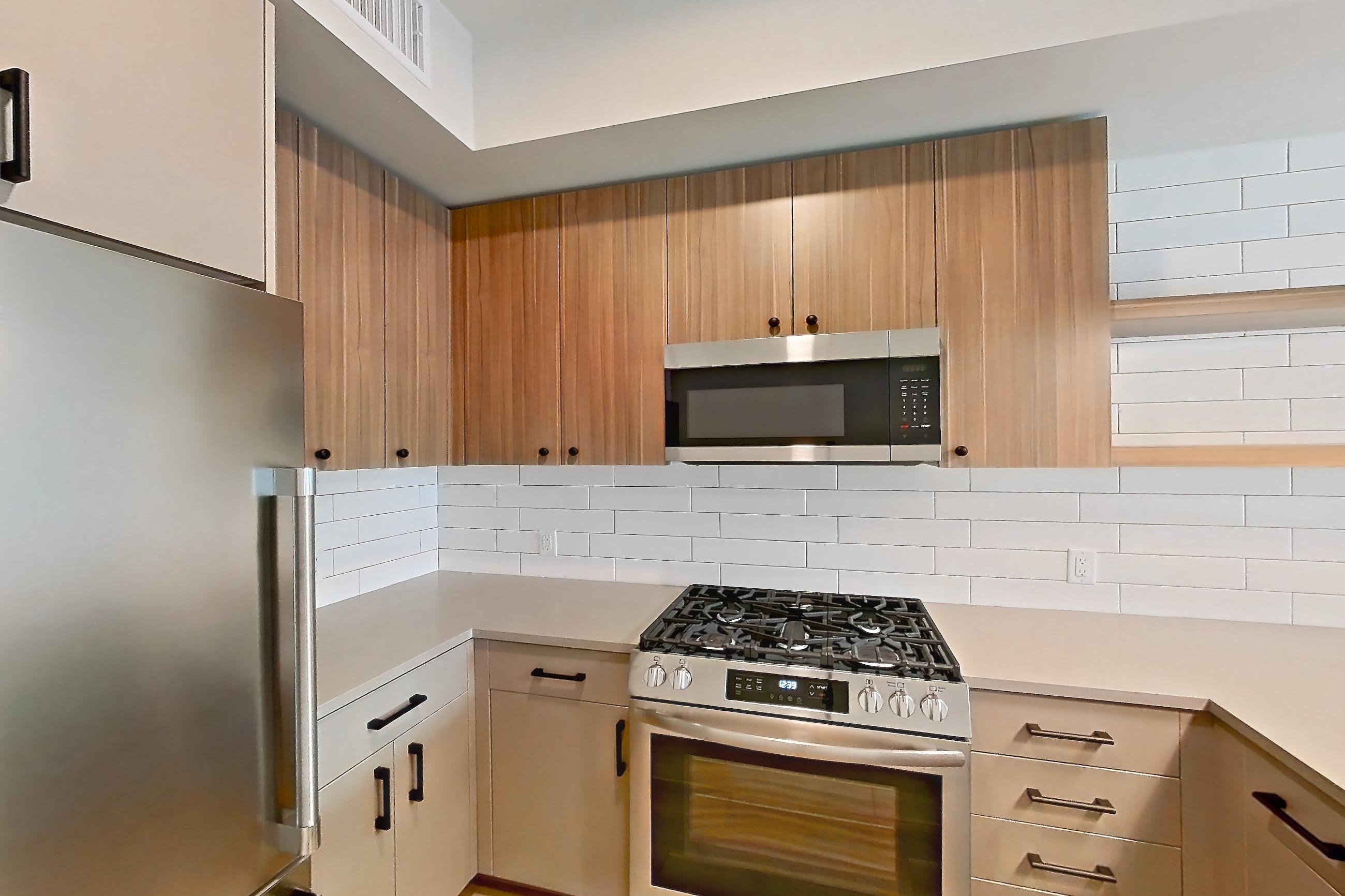 Kitchen with dishwasher, gas range, light countertops, light wood-finish flooring, microwave, oven/range, refrigerator, and stainless steel appliances, Apartment 442 at The Myles