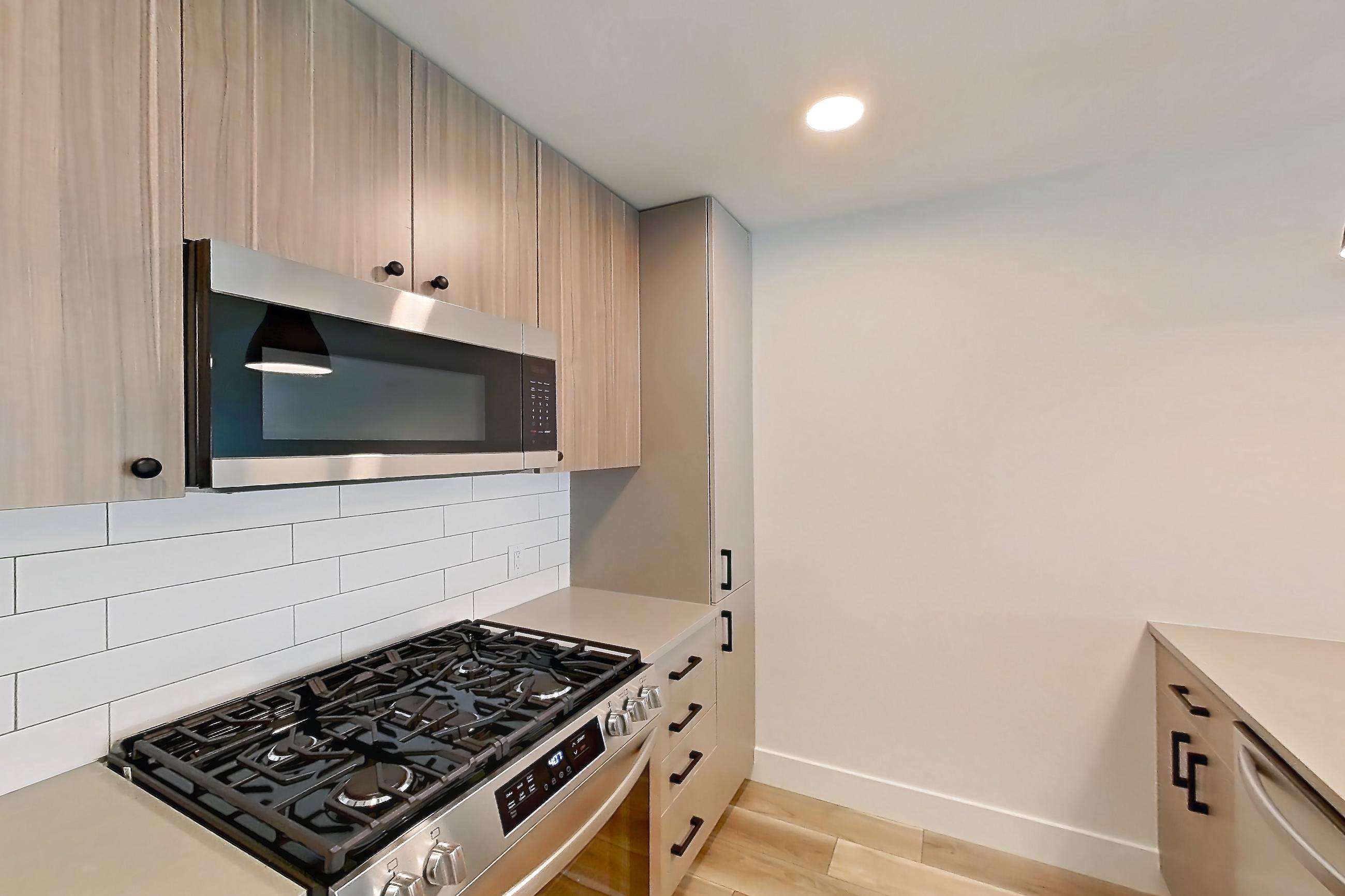 Kitchen with dishwasher, gas range, light countertops, light wood-finish flooring, microwave, oven/range, refrigerator, and stainless steel appliances, Apartment 446 at The Myles