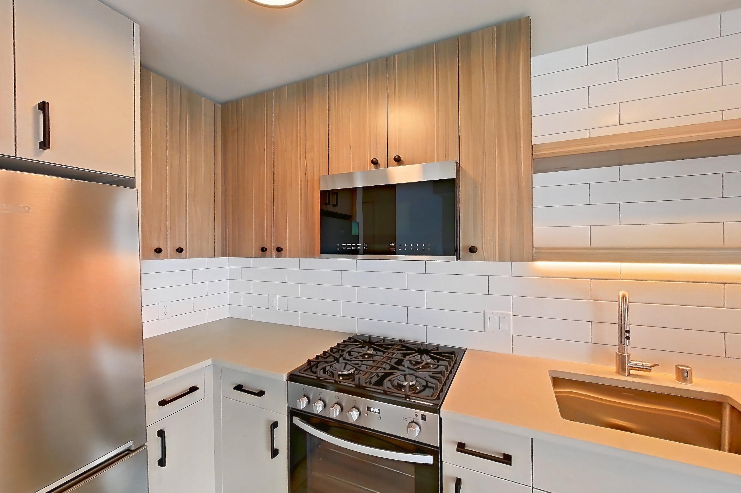 Kitchen with dishwasher, gas range, light countertops, light wood-finish flooring, oven/range, refrigerator, and stainless steel appliances, Apartment 445 at The Myles